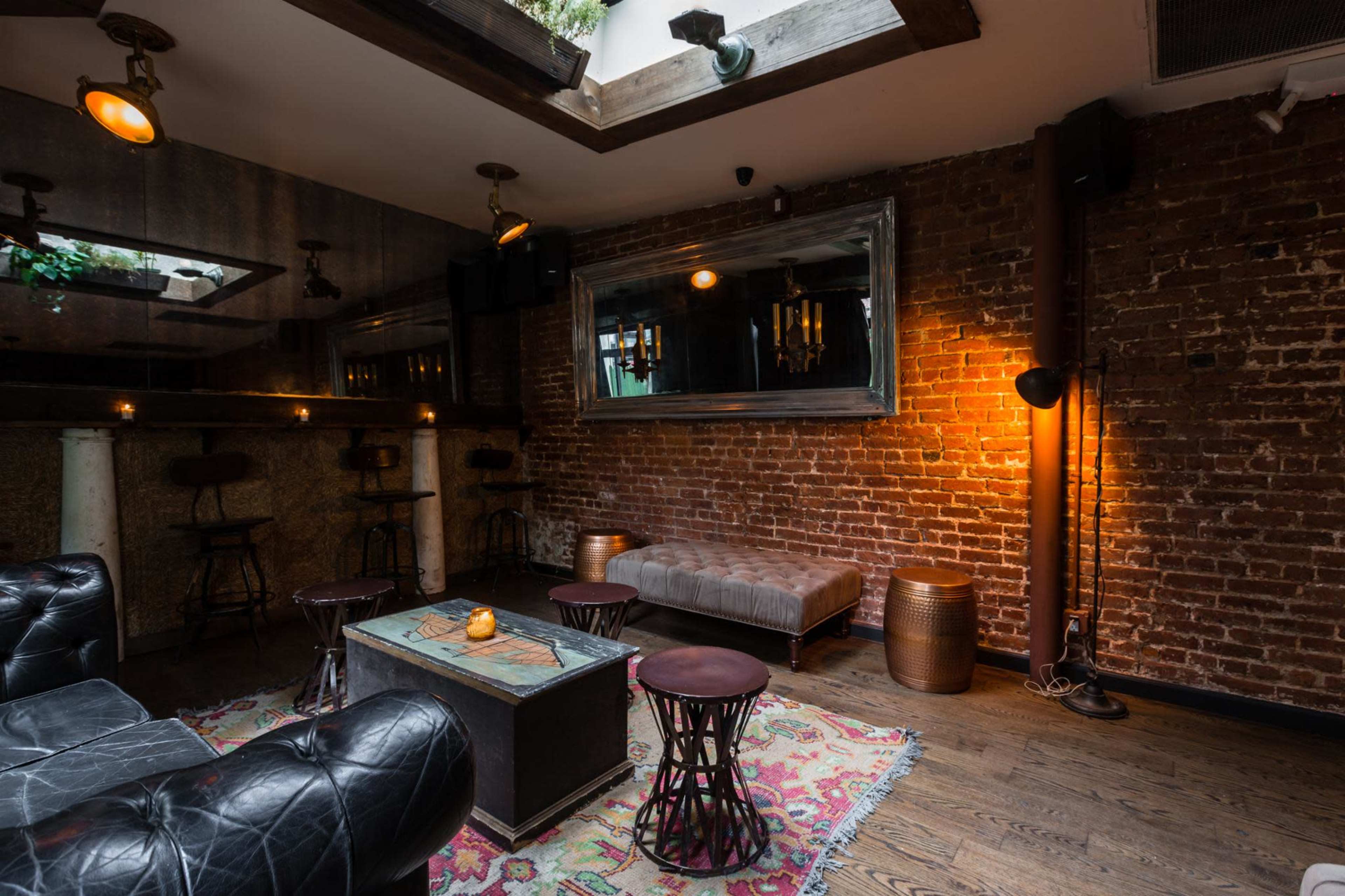 A cozy lounge area with exposed brick walls, a low coffee table, seating on a patterned rug, and warm lighting fixtures.