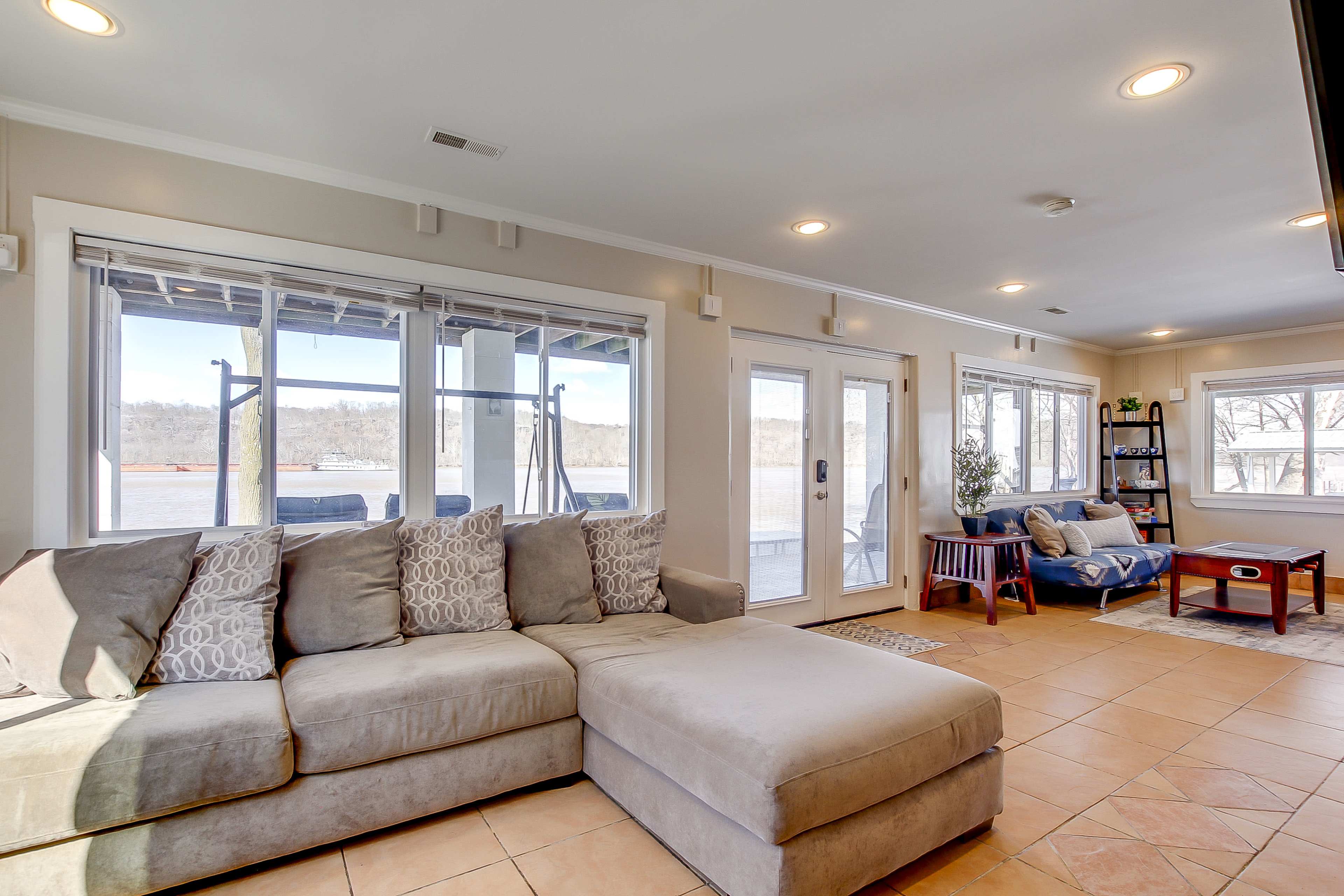 A spacious living room with a large sectional sofa, a coffee table, and windows overlooking a body of water.