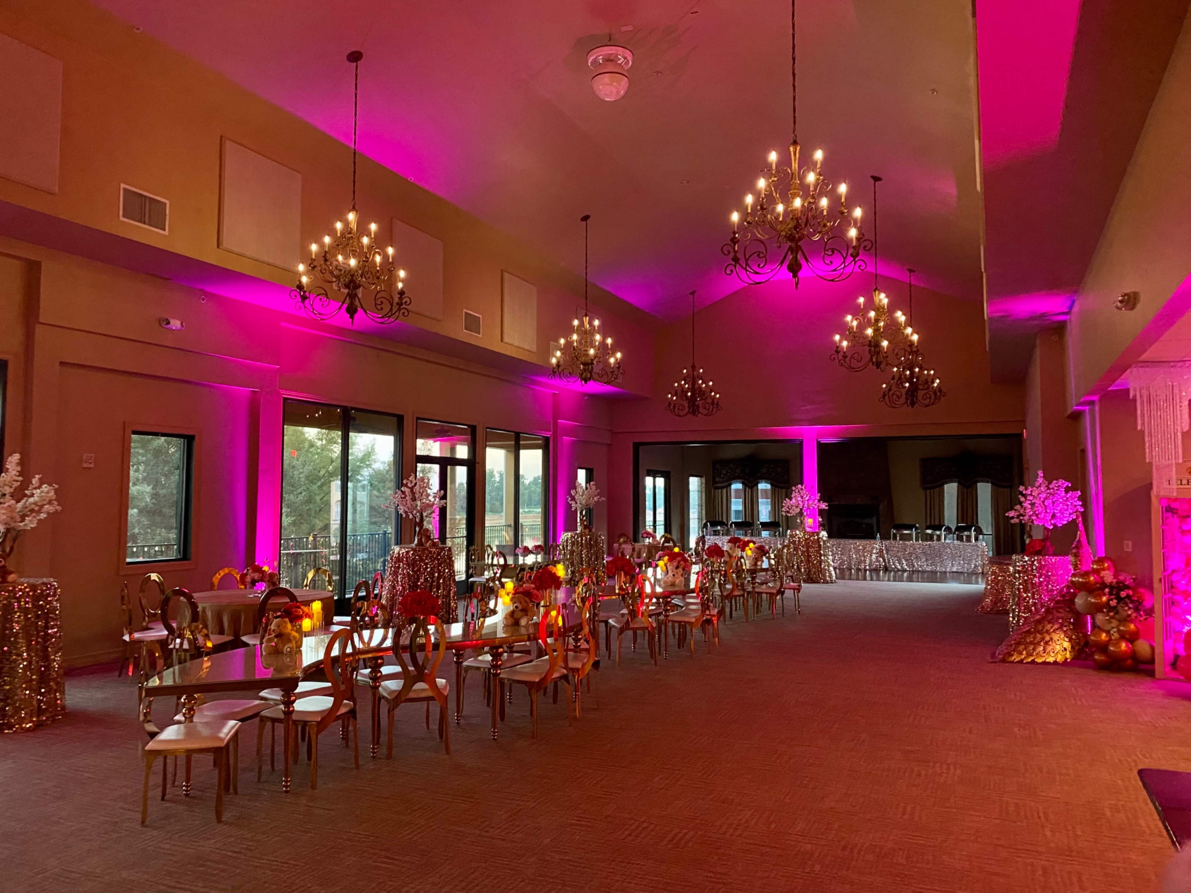 A banquet hall decorated with pink lighting, chandeliers, and ornate tables set up for an event.