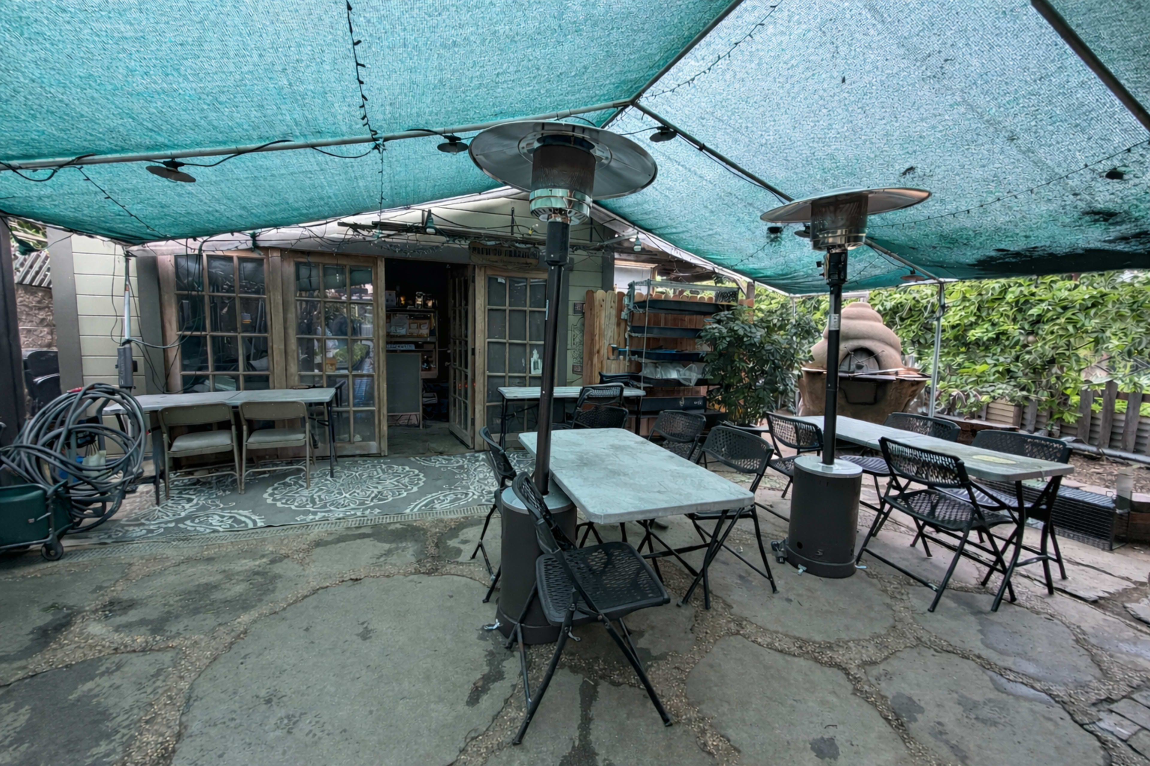 The image shows an outdoor patio area with tables and chairs, covered by a blue tarp, adjacent to a building.