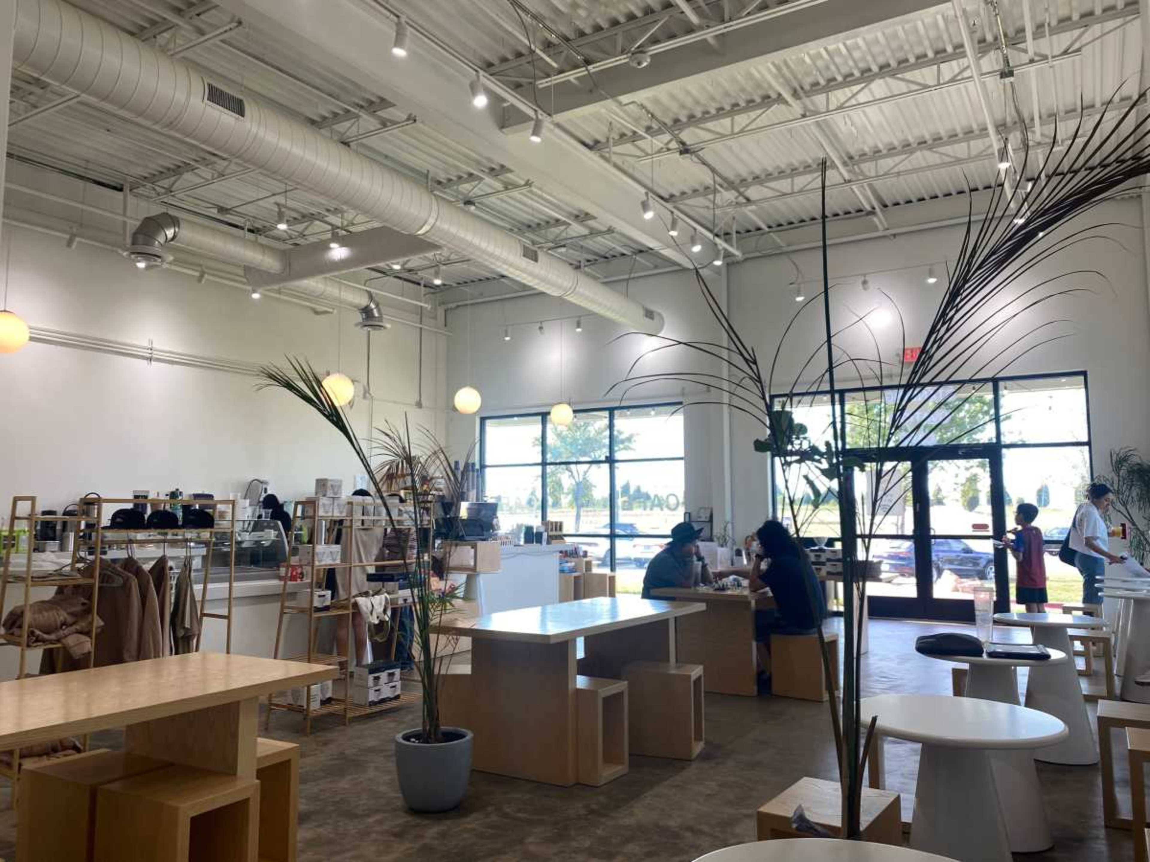 The image shows a modern café interior with light-colored furnishings, large windows, and a few patrons seated at tables.