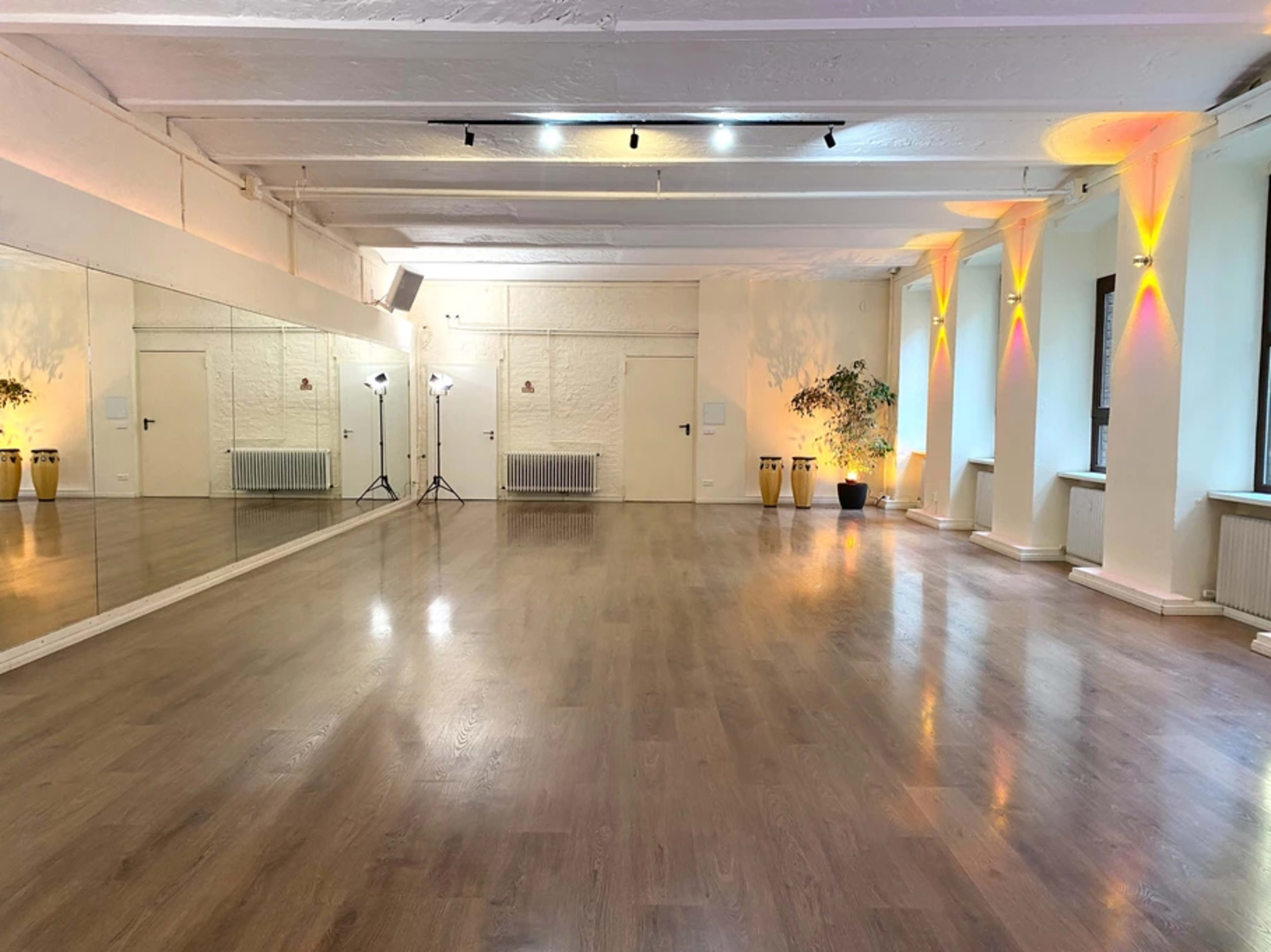 An empty dance studio with wooden floors, white walls, mirrors, and soft lighting.
