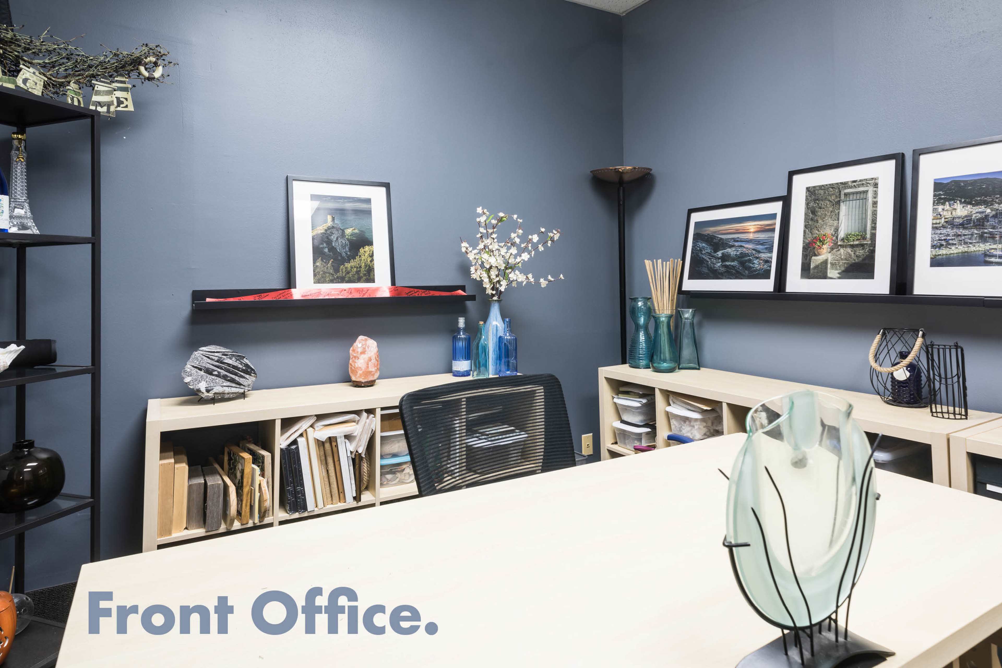 A front office with dark gray walls, modern shelving units filled with books and decorative items, and a wooden desk with a black chair.