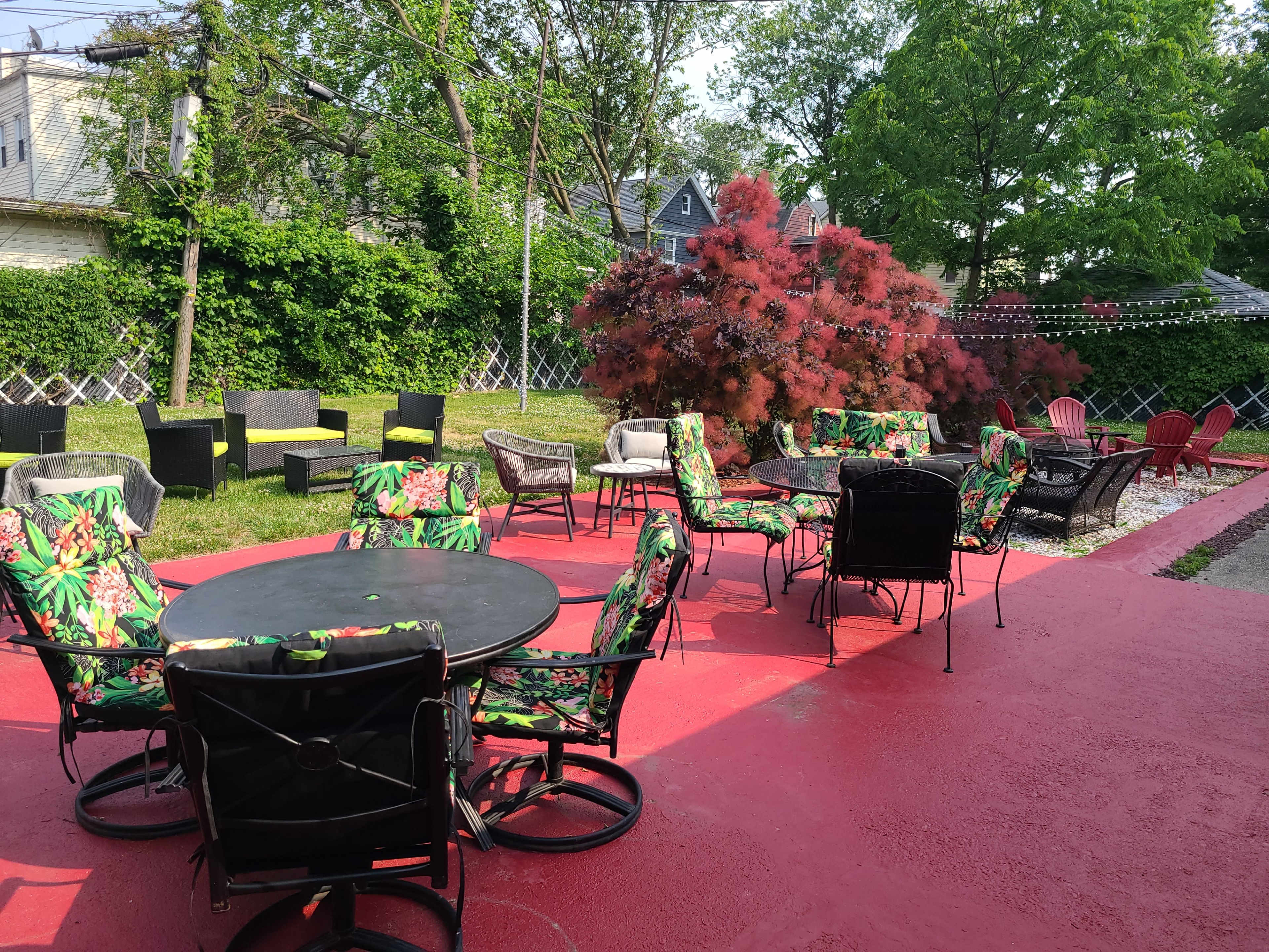 A patio area with colorful chairs and tables arranged on a red surface, surrounded by greenery and decorative plants.