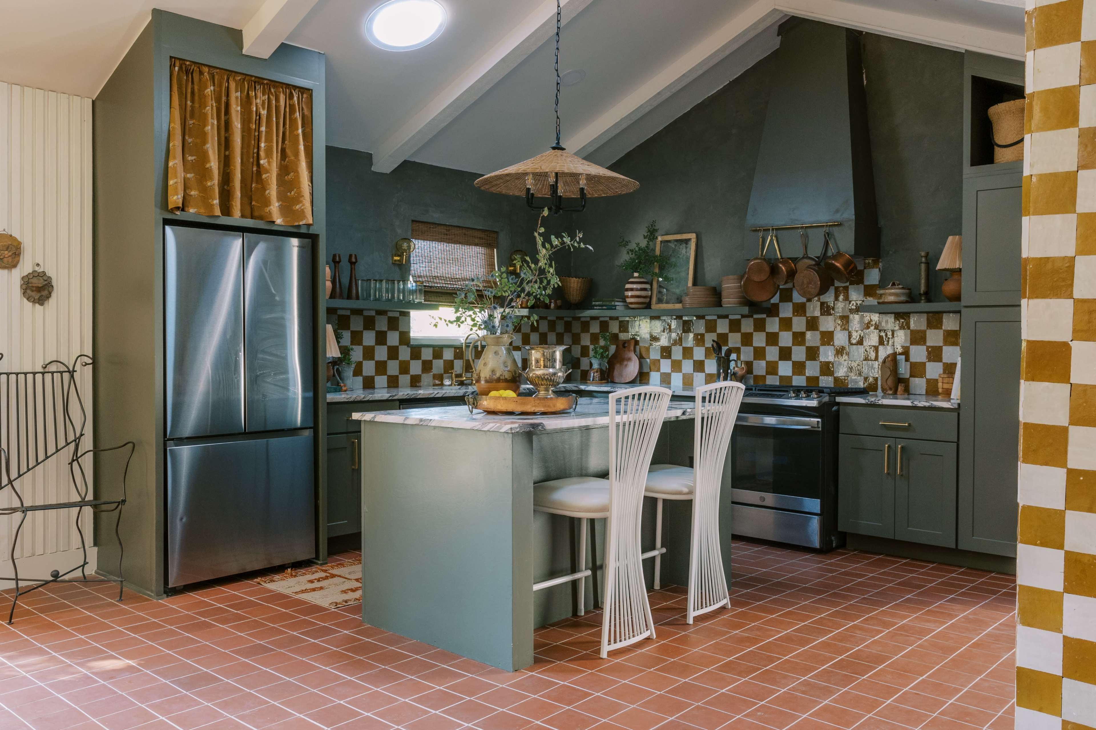 A kitchen featuring a green island with two white bar stools, a checkered backsplash, and stainless steel appliances.