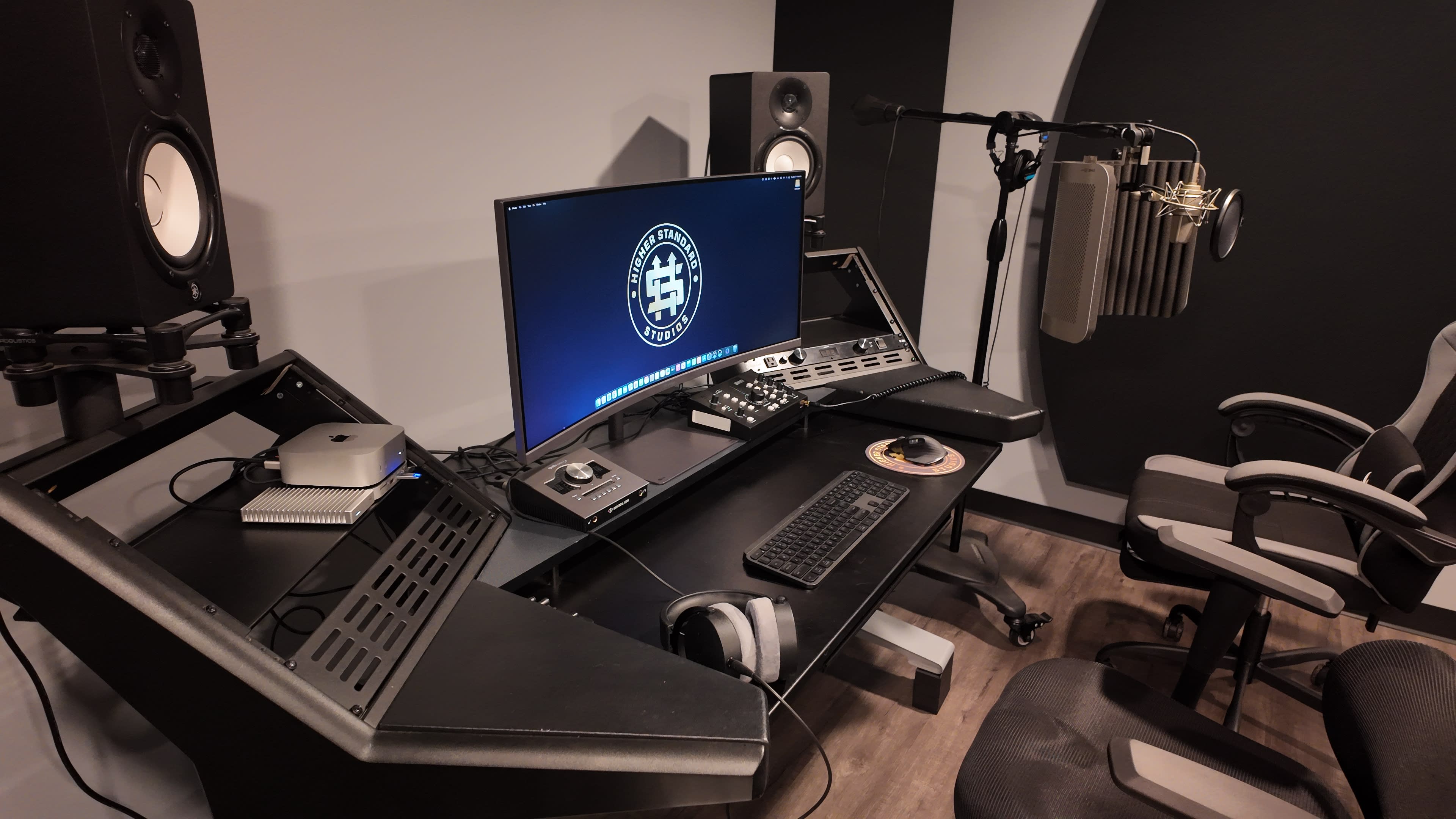 The image shows a modern audio recording studio setup with a computer monitor, audio interface, studio monitors, and a microphone with a pop filter.