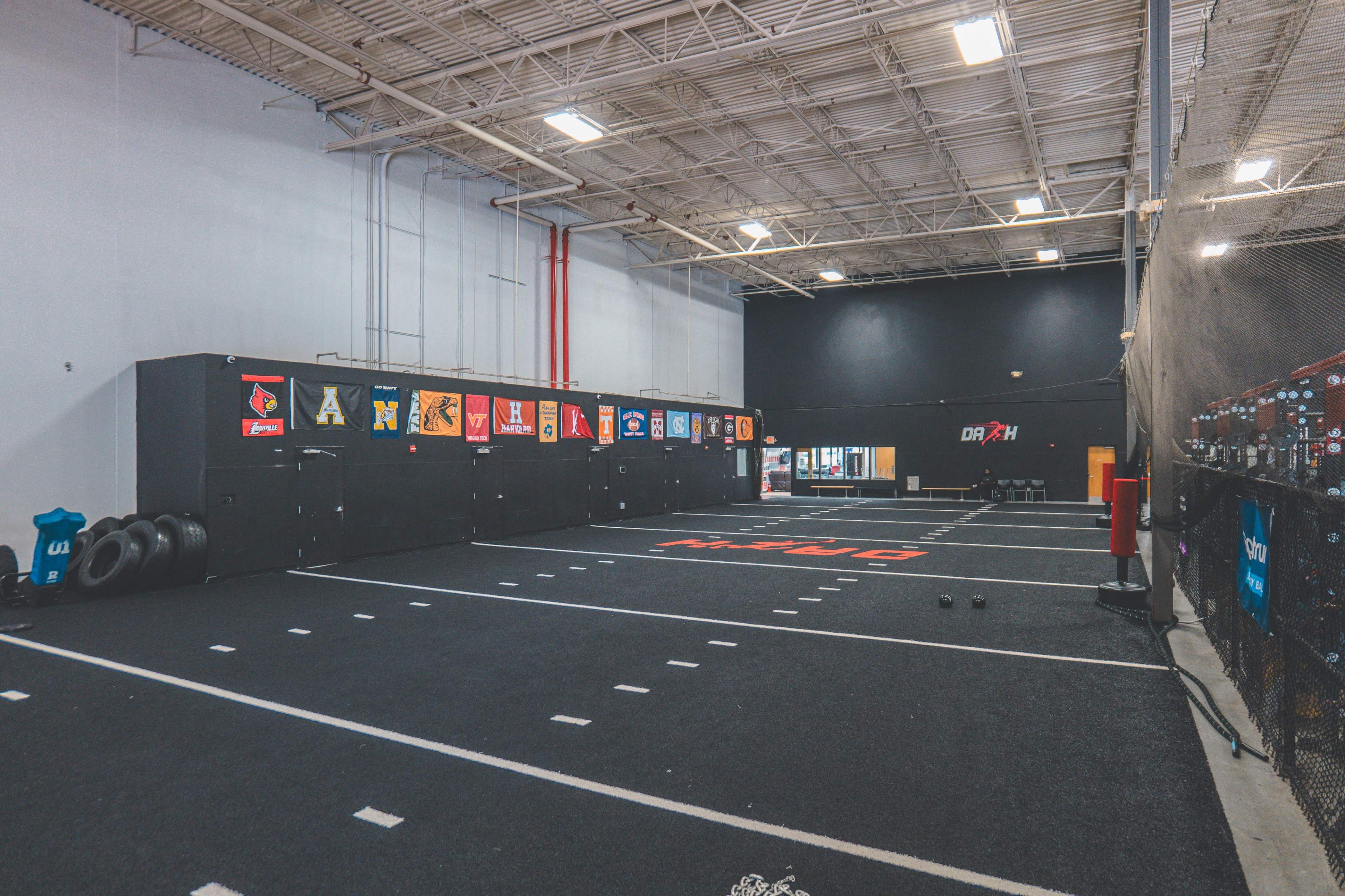 A training facility with a rubberized floor, marked lanes, and walls decorated with team banners and equipment, including tires and weights.