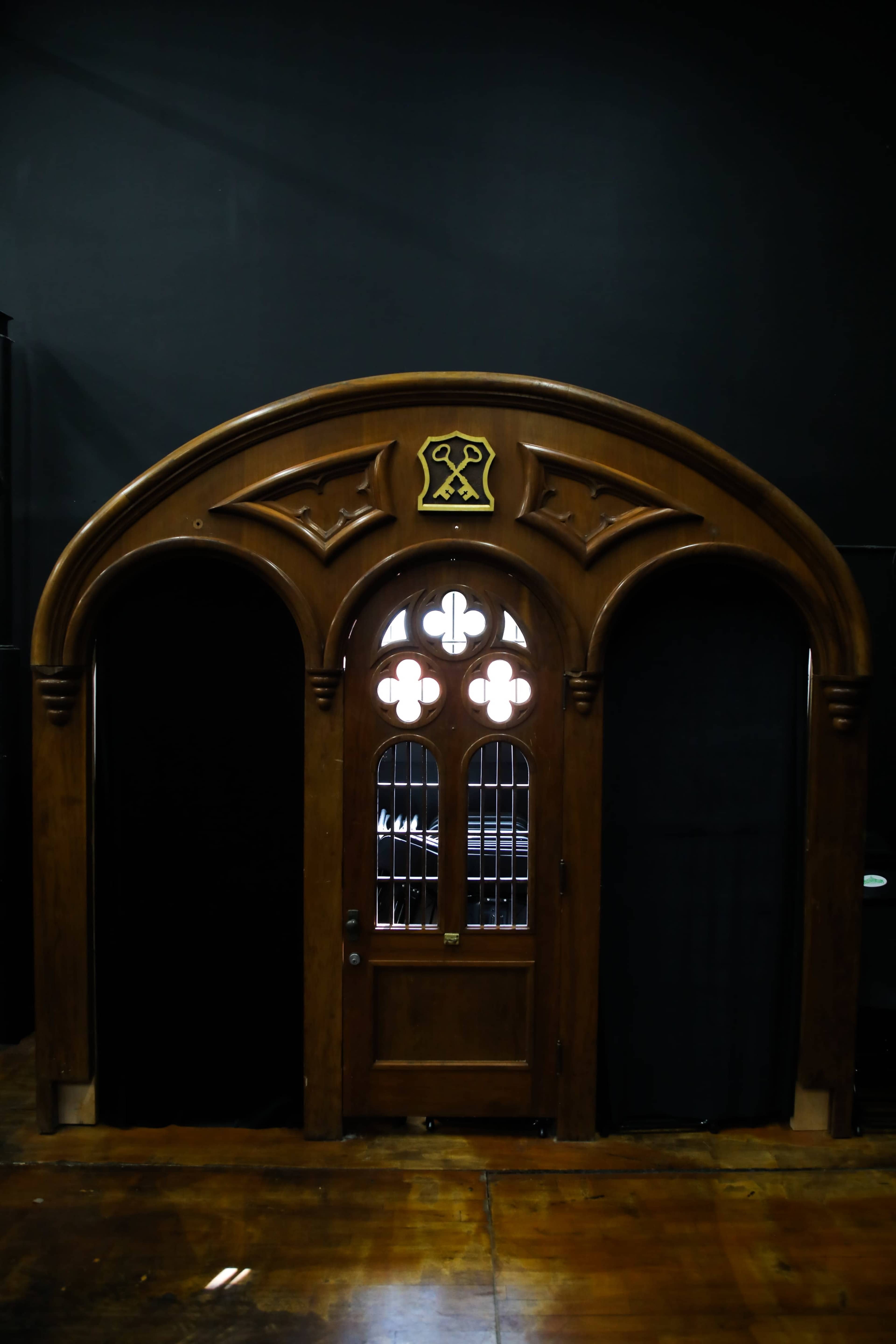 The image shows an ornate wooden door with decorative architraves and a symbol above it, set against a dark background.