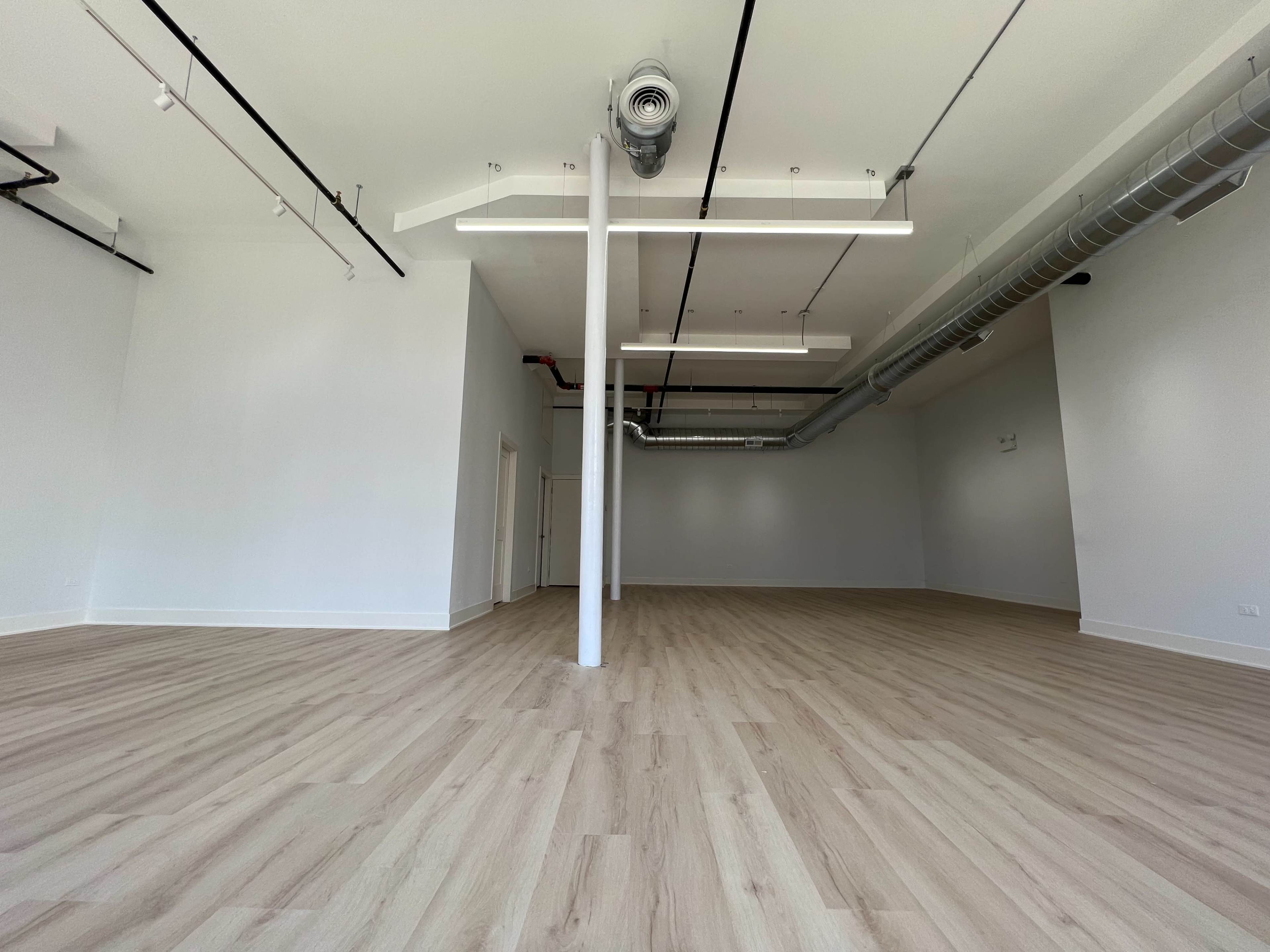 A spacious, empty room with light wooden flooring and white walls.