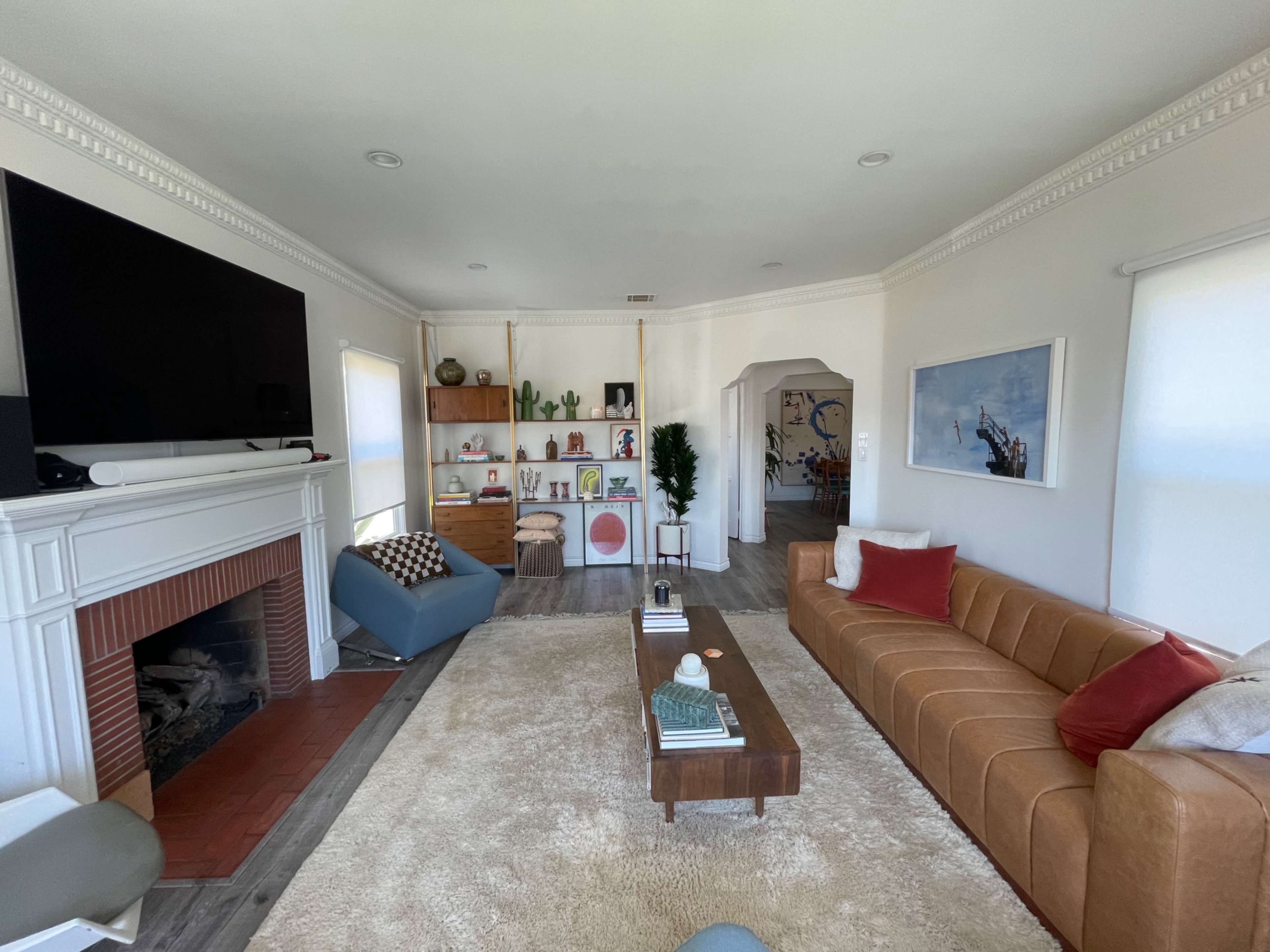 A modern living room features a large brown sofa, a wooden coffee table, a fireplace, and a wall-mounted television, with shelves displaying plants and decor in the background.
