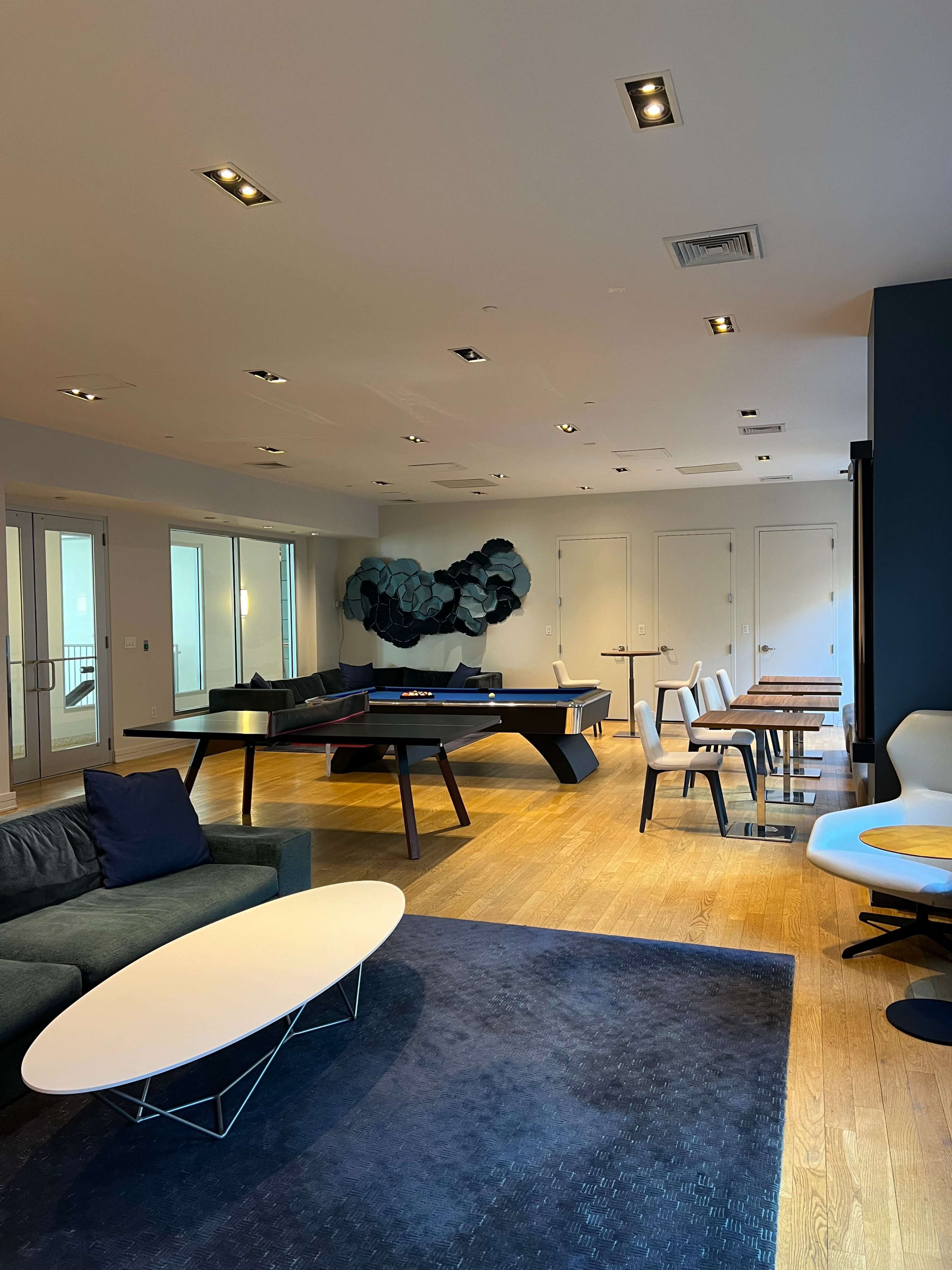 A modern lounge area features stylish seating, a central coffee table, and various tables arranged throughout the space.