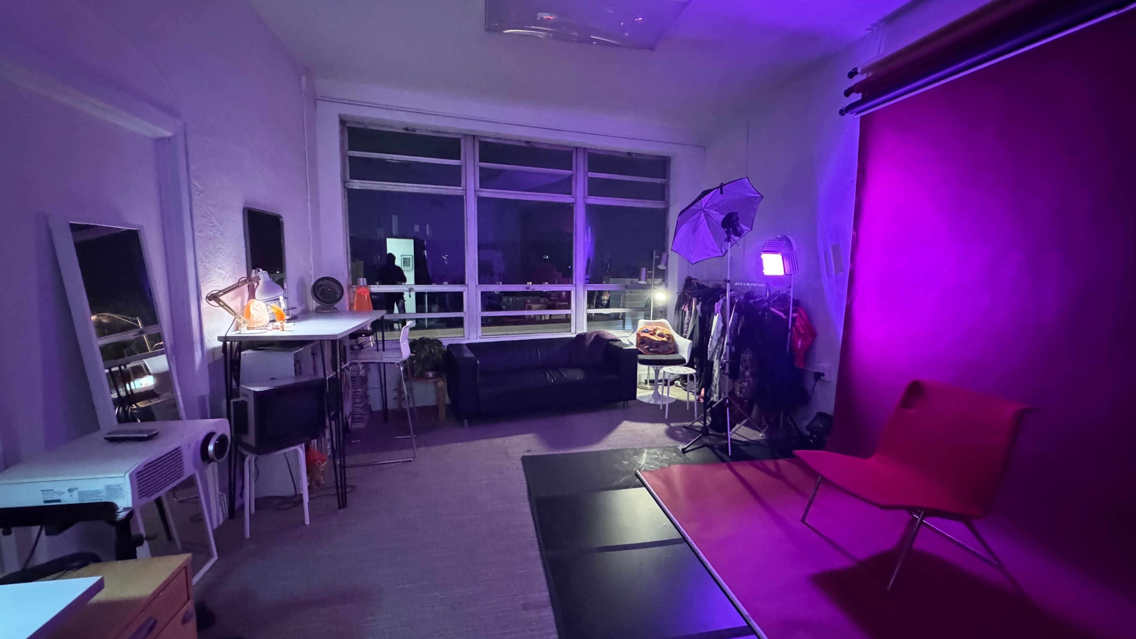 The image shows a room with purple lighting, featuring a black couch, a photography backdrop, and various equipment arranged around the space.