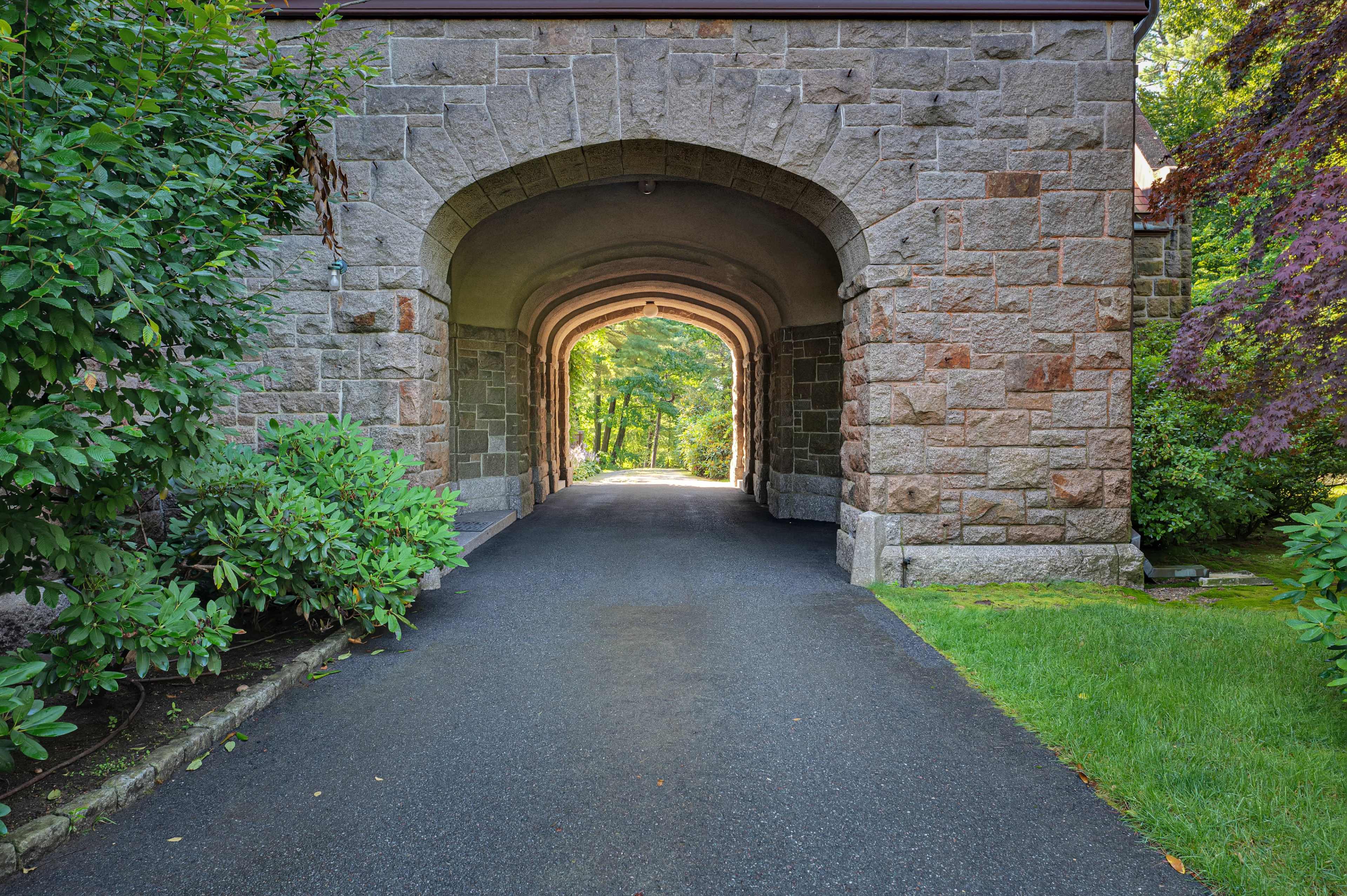 The image shows a stone archway leading to a tree-lined pathway.