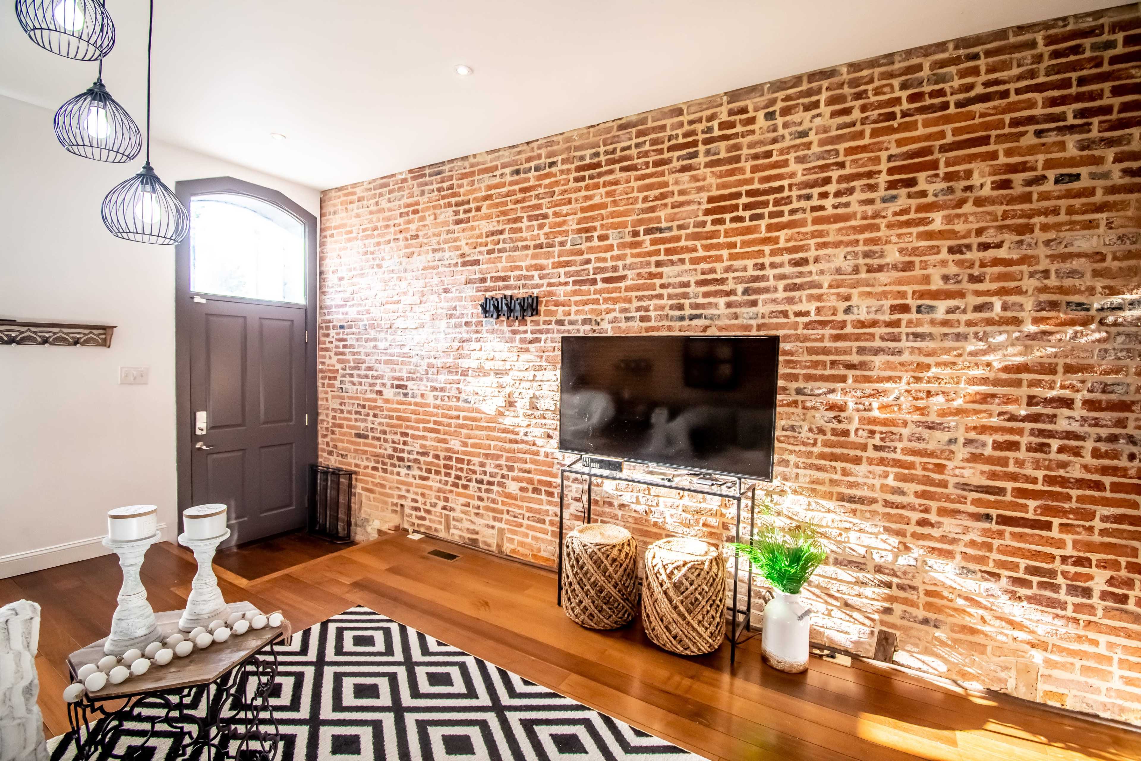 A cozy interior with a brick wall, a television on a stand, decorative baskets, and a small plant beside the entrance door.