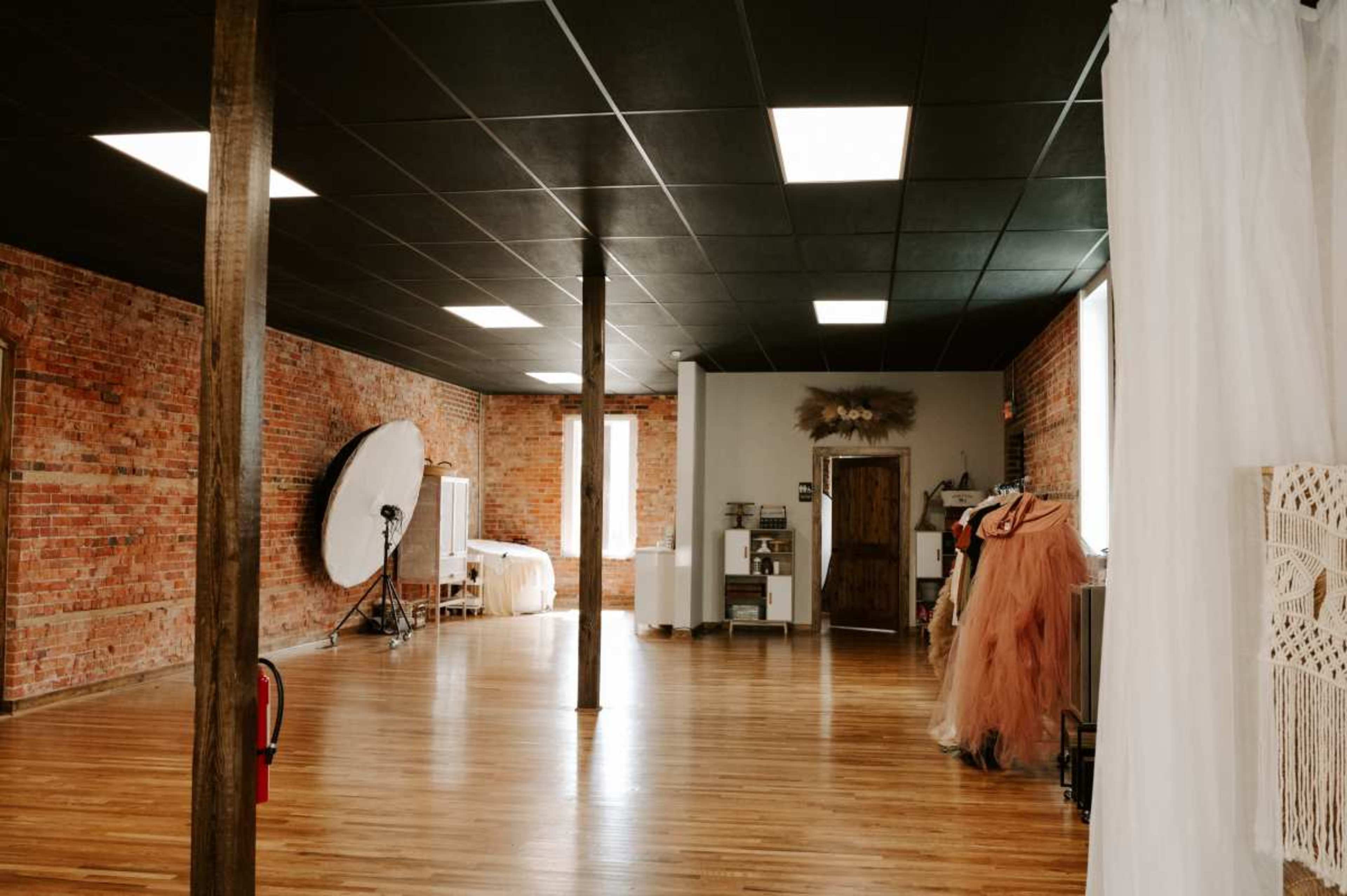 A spacious photography studio with exposed brick walls, wooden floors, and various props and clothing arranged around the room.