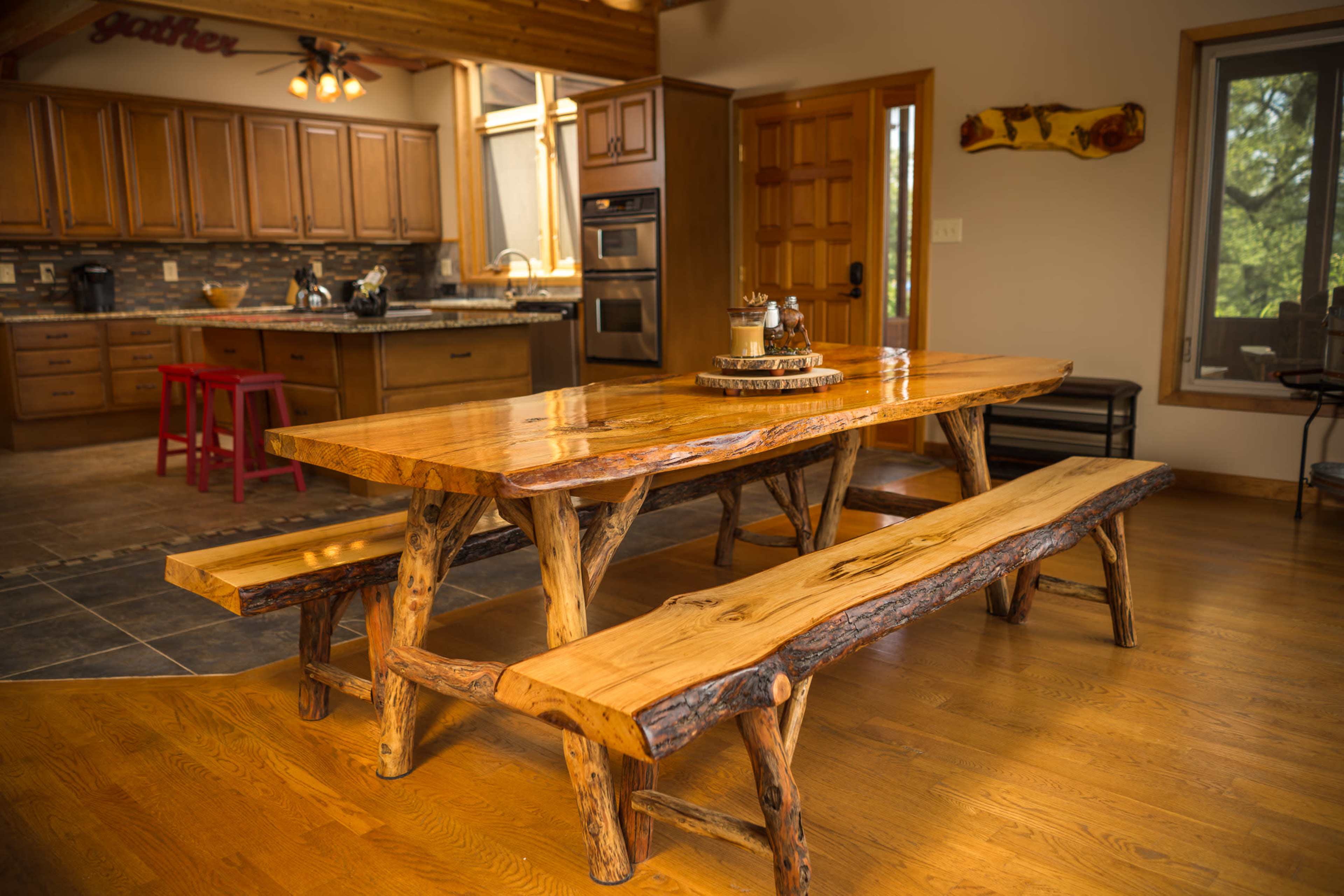 A wooden dining table with matching benches in a spacious kitchen area featuring cabinetry and modern appliances.