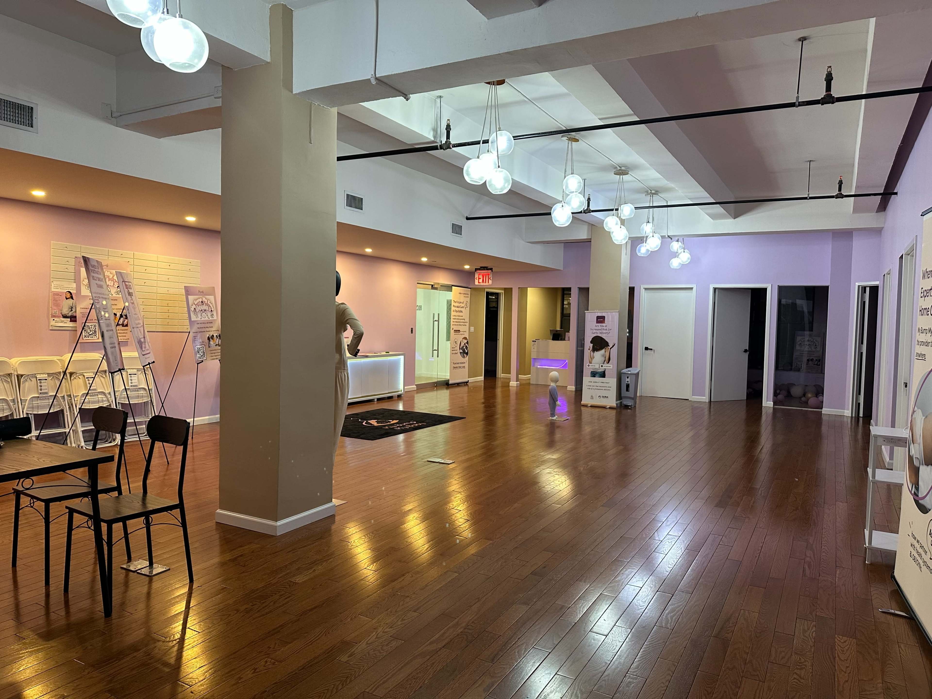 The image shows a spacious, well-lit interior with polished wooden floors, featuring modern lighting fixtures and empty seating areas.