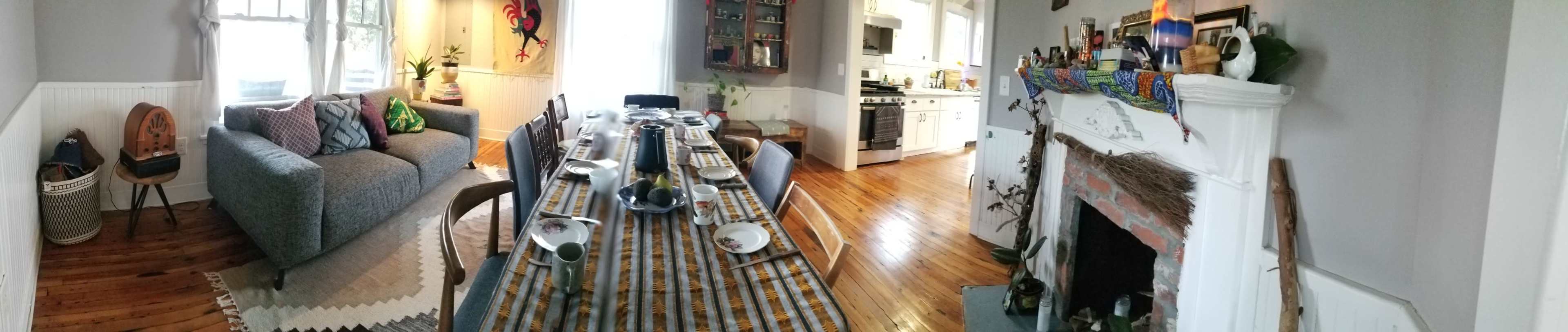 A cozy living and dining area with a large table set for a meal, a gray sofa, and a decorated fireplace.
