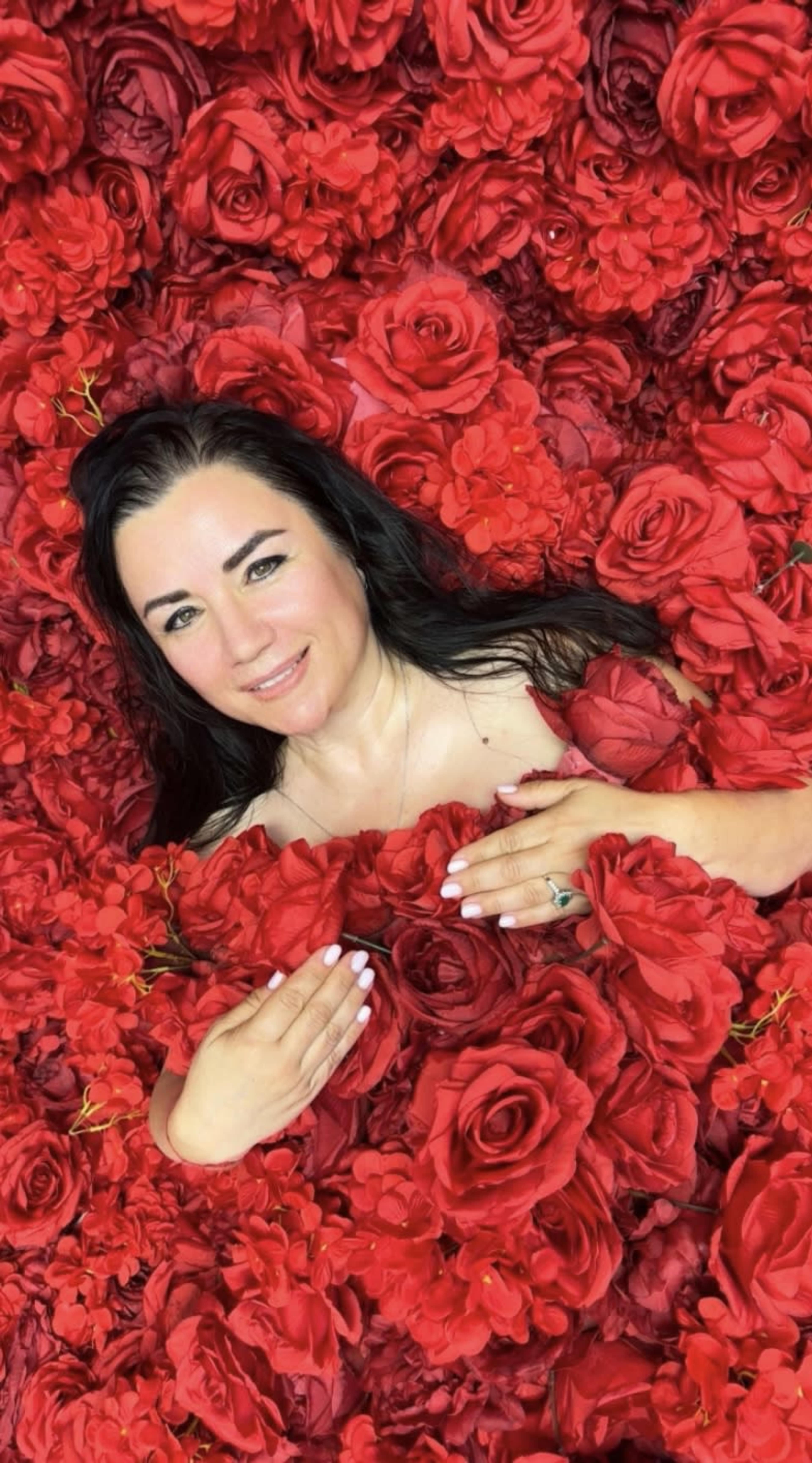 A woman with long dark hair is lying among an array of red roses.