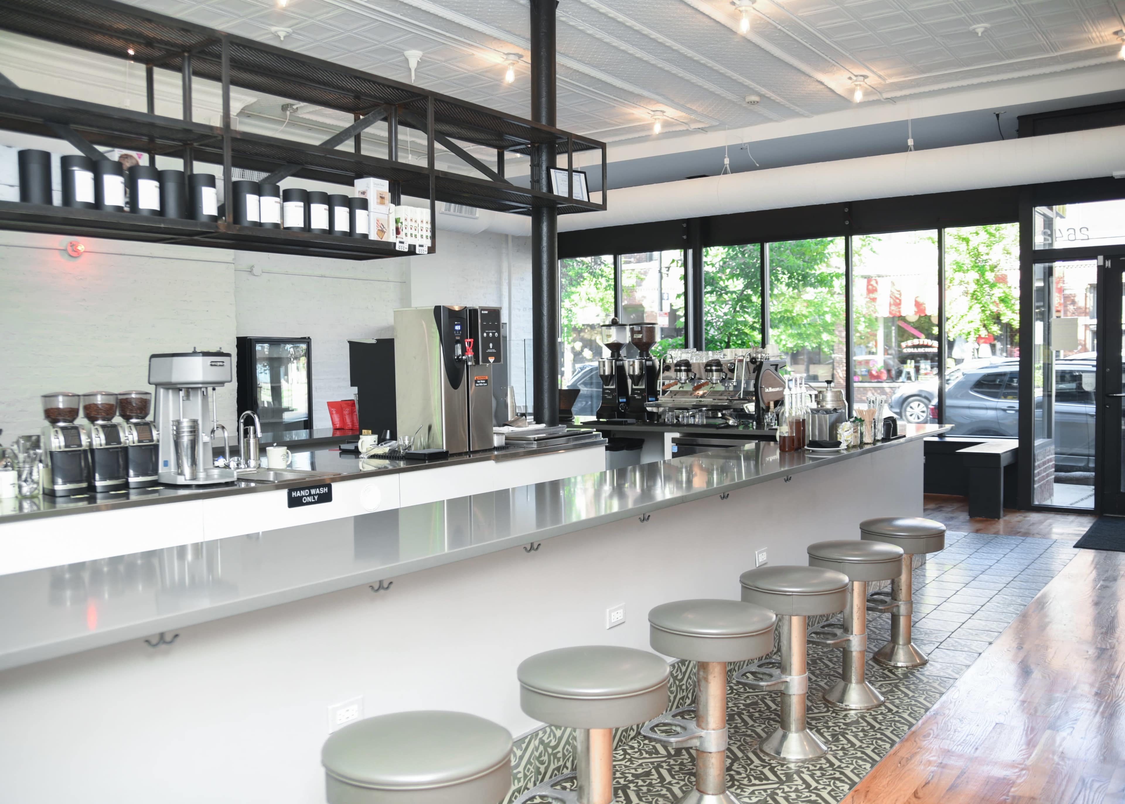 A modern café interior with a sleek counter, several bar stools, and coffee equipment lined up behind the counter.