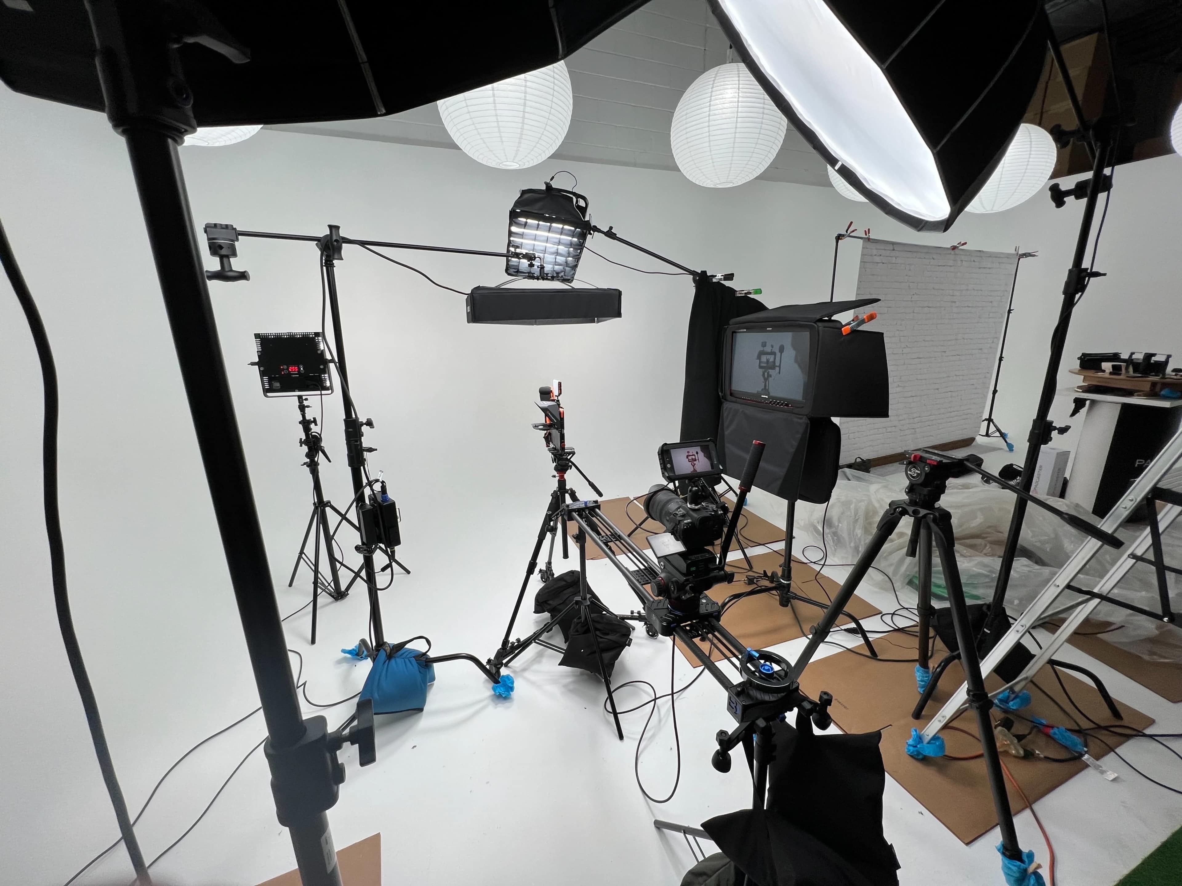 A photography studio setup featuring multiple cameras, lighting equipment, and a backdrop.