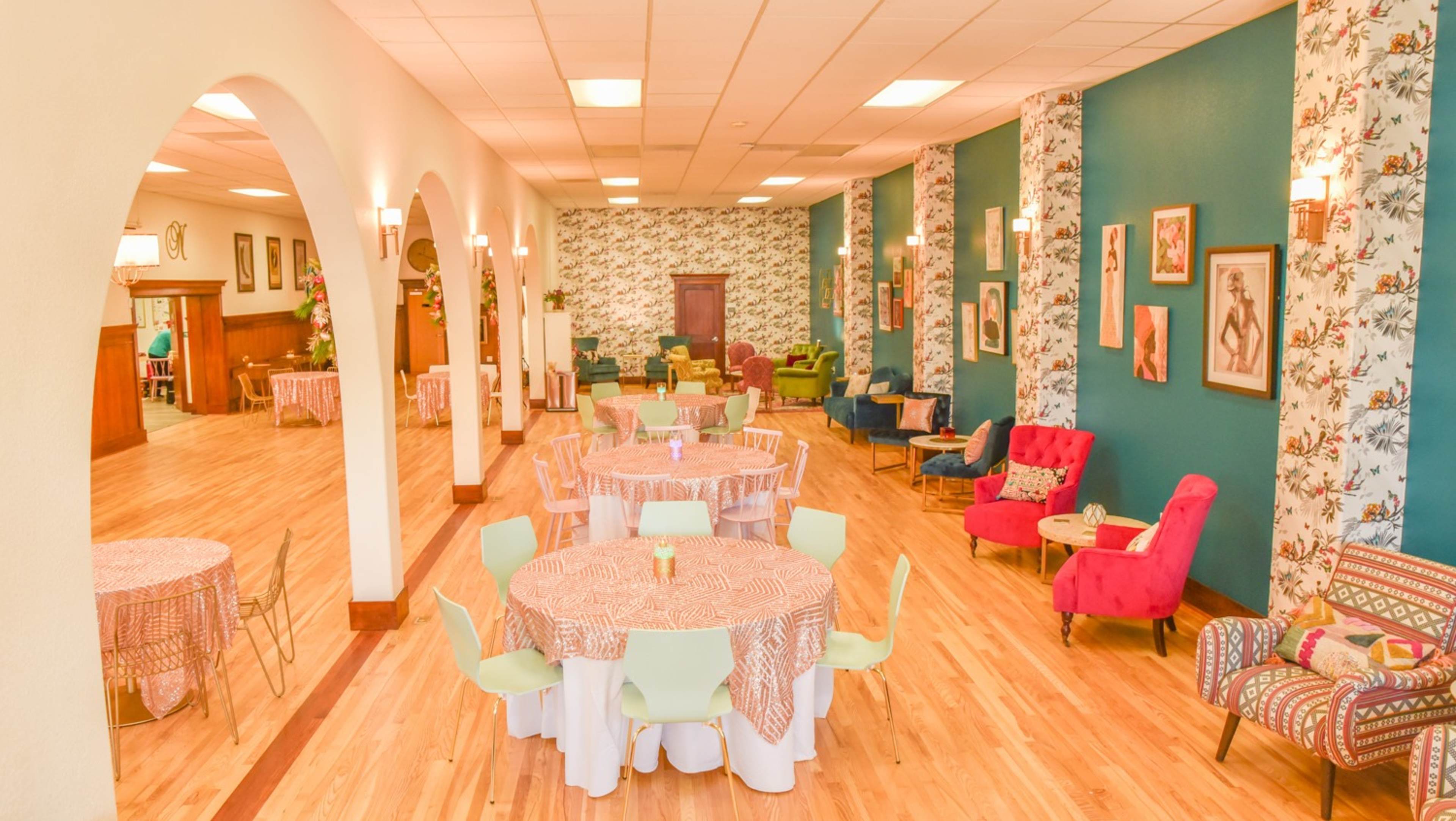 A spacious event hall with colorful furniture, floral wallpaper, and tables set with patterned tablecloths.