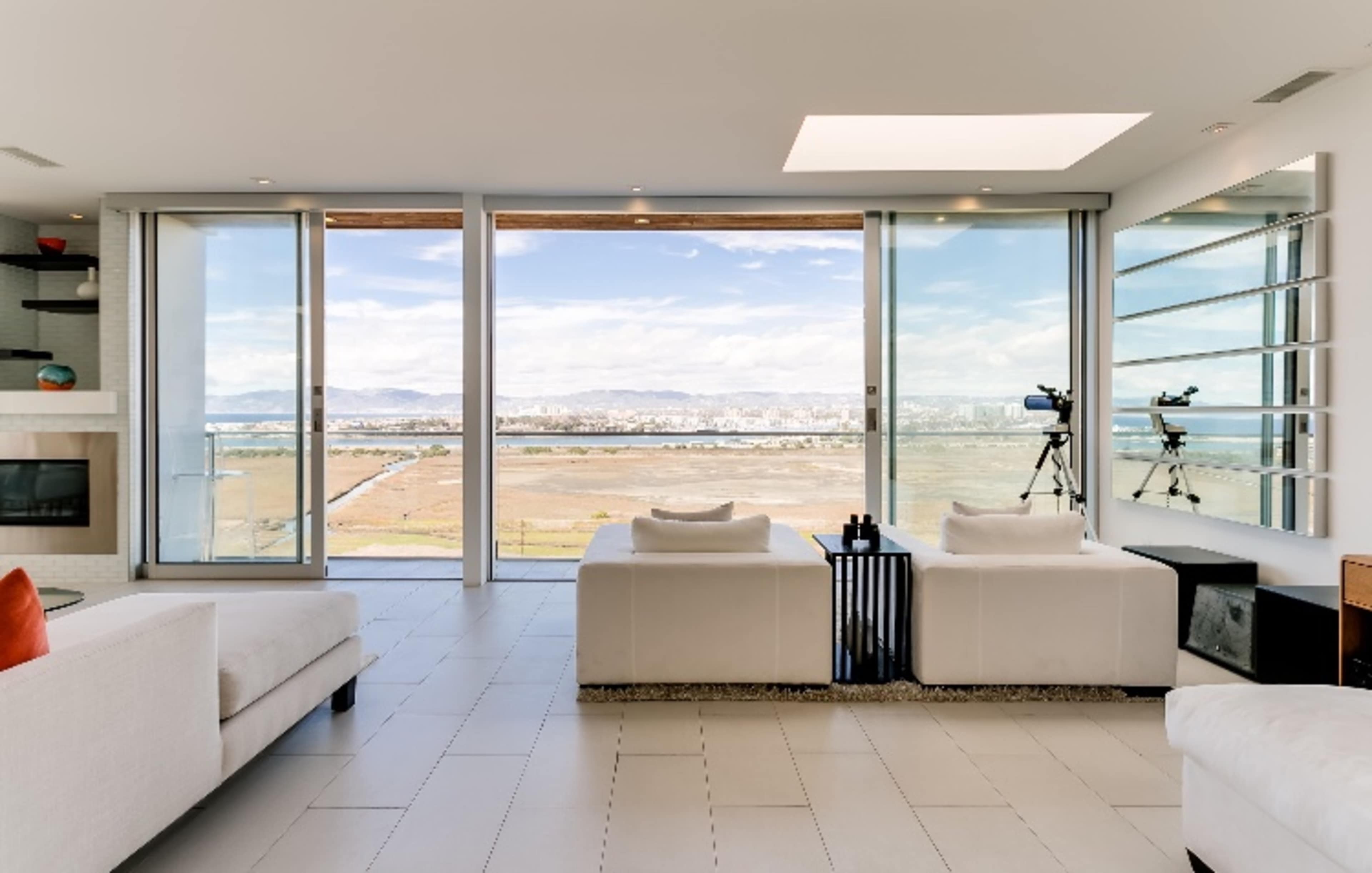 A modern living room with large glass windows offering a view of the landscape and city beyond.
