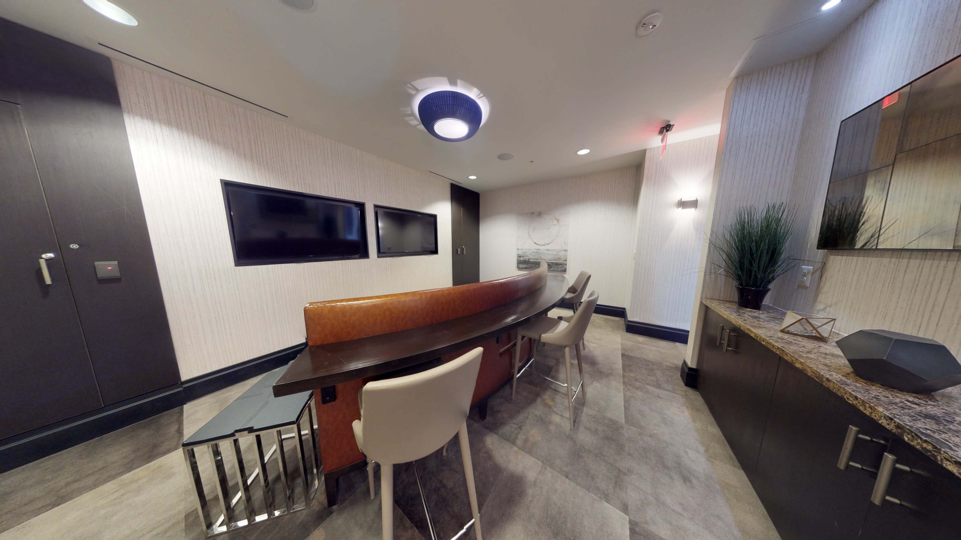 A small conference room with a curved table, chairs, and two mounted flat-screen TVs on the wall.