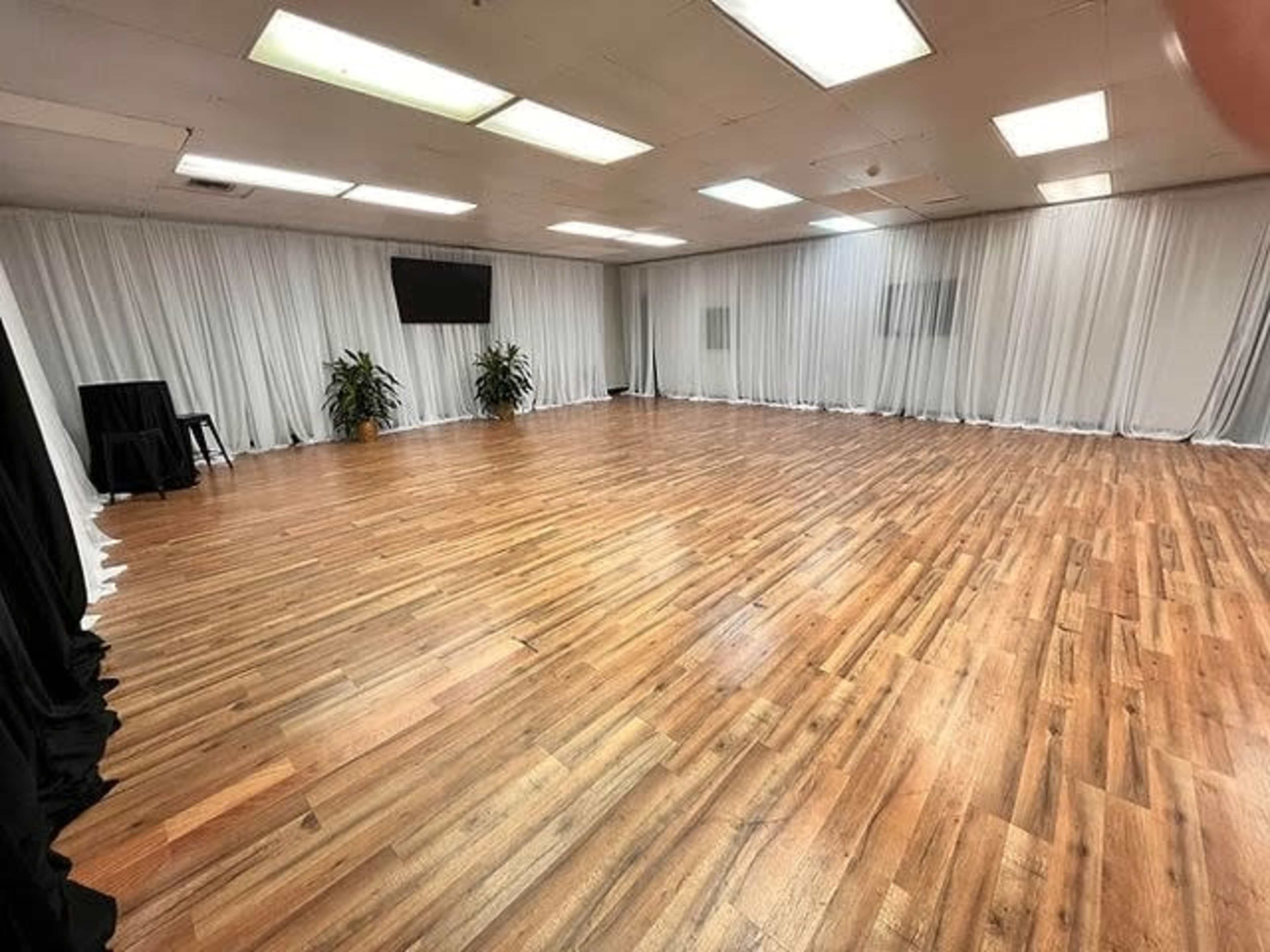 A spacious indoor room with wooden flooring, white drapes along the walls, and a large, empty area.