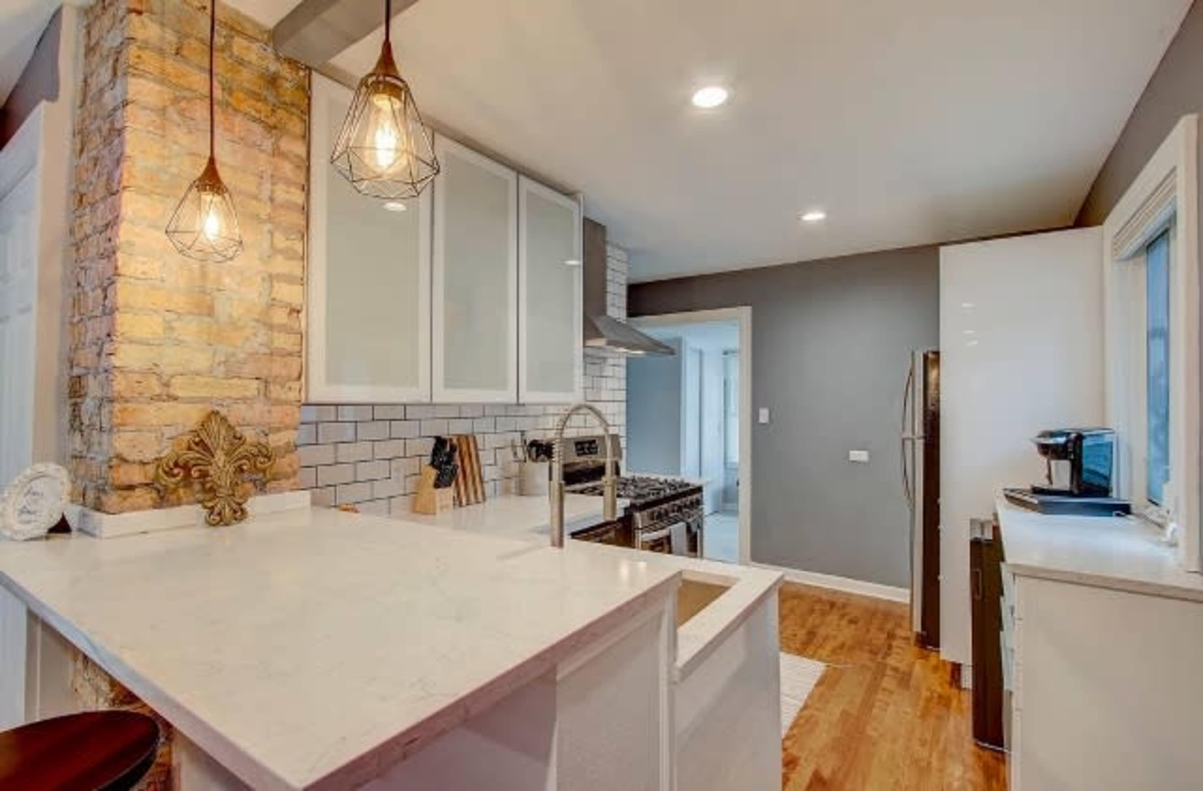 A modern kitchen featuring a central island with a white countertop, pendant lights, and stainless steel appliances against a backdrop of gray and white walls.