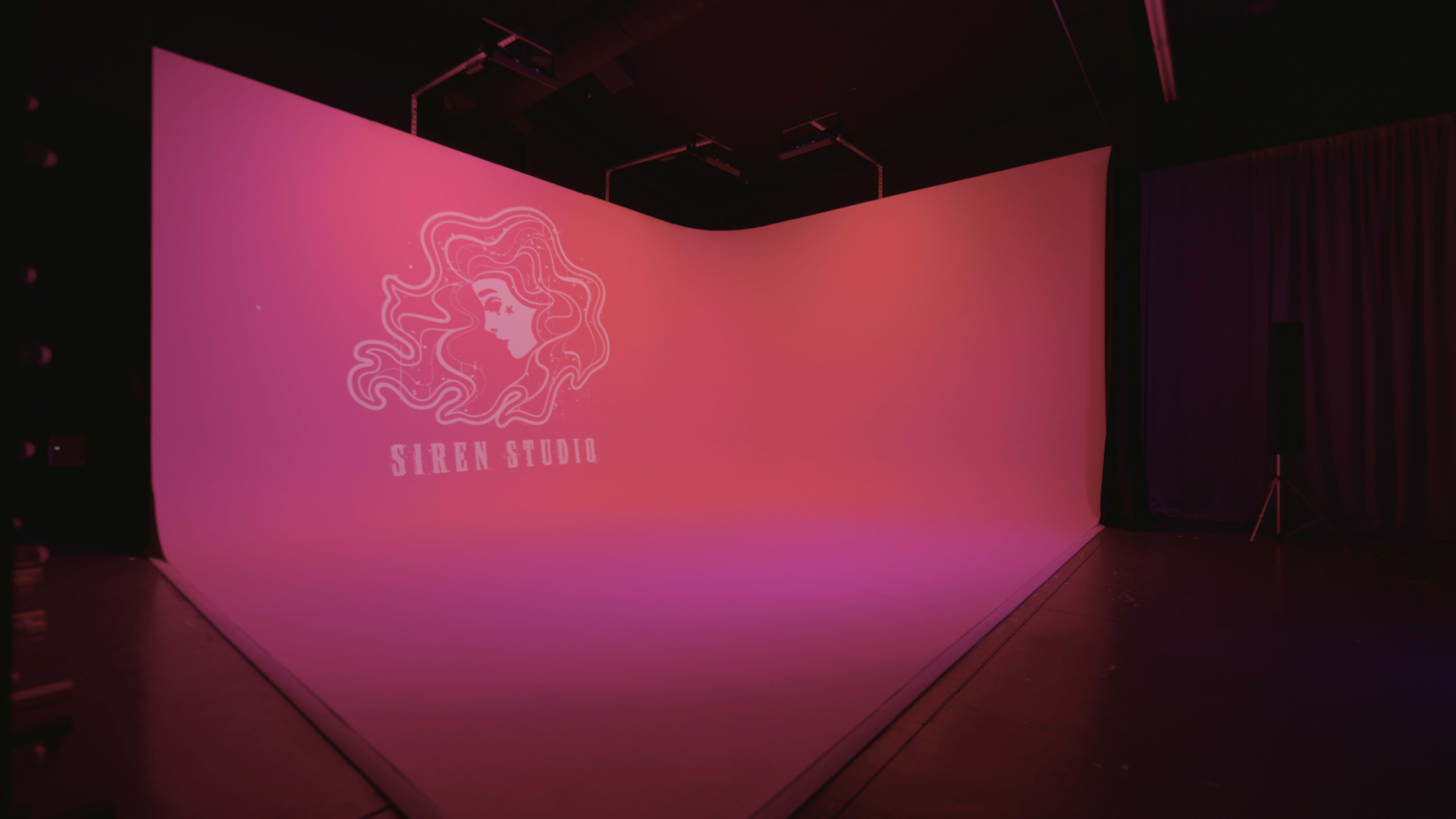 A large studio space with a gradient pink backdrop and the logo "Siren Studio" projected on it.