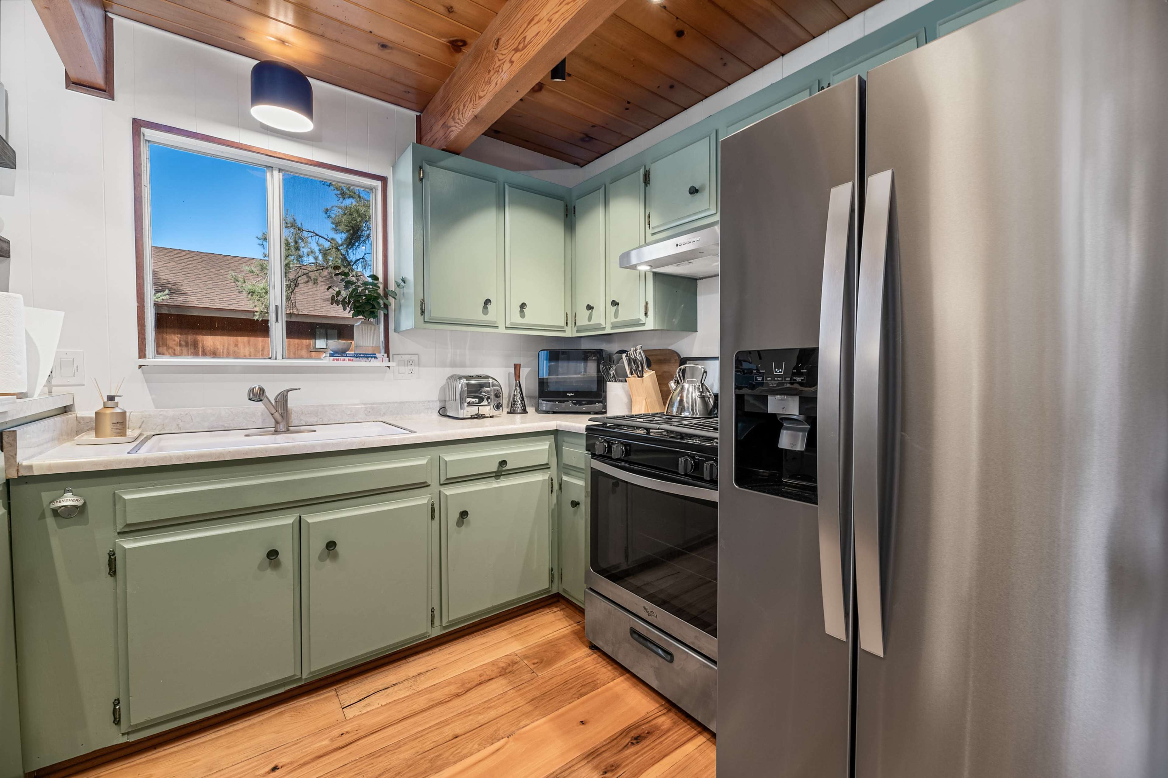 A kitchen with green-painted cabinets, a stainless steel refrigerator, and wooden flooring.