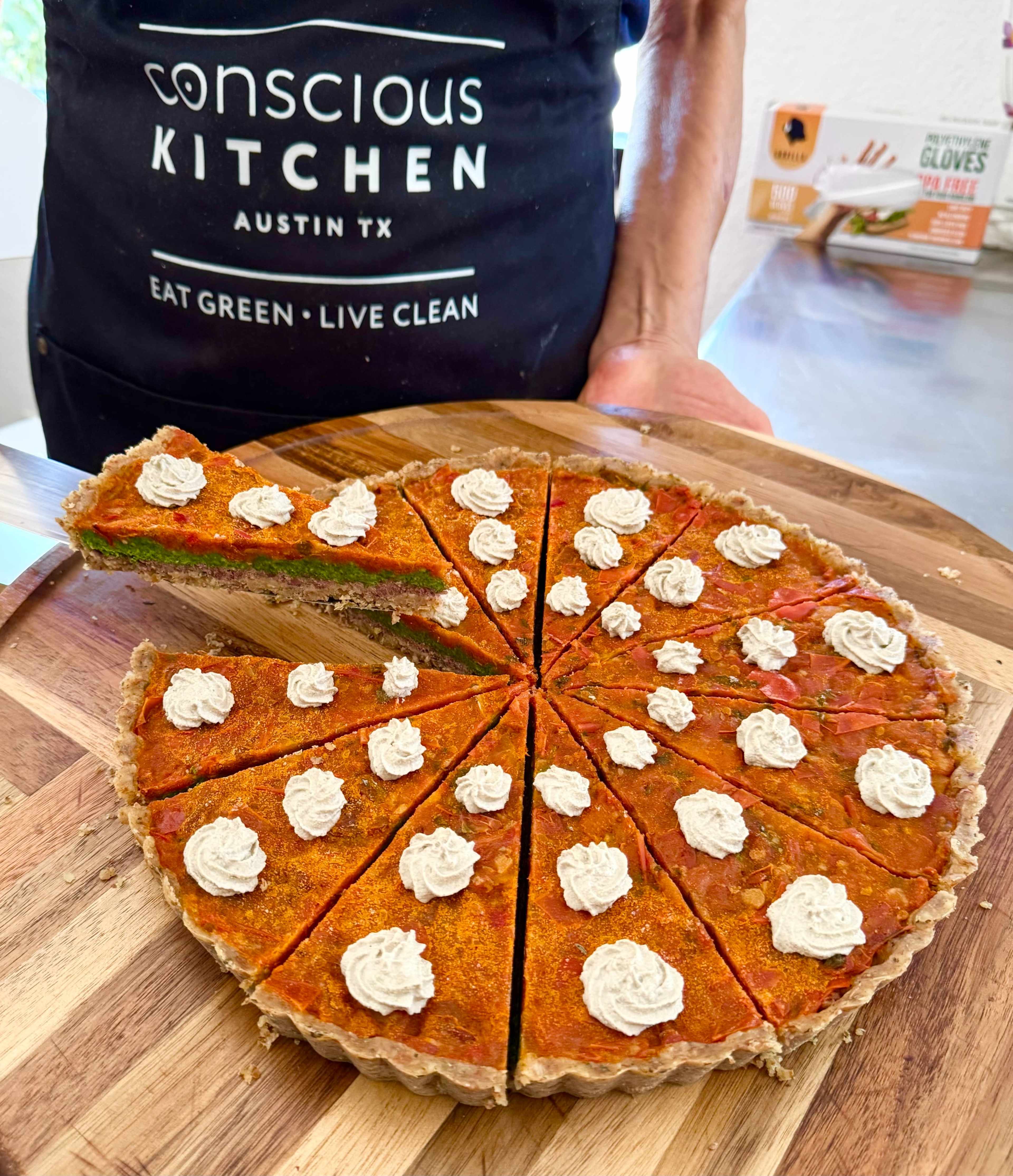 A round, sliced tart with a colorful filling is displayed on a wooden board, topped with dollops of cream.