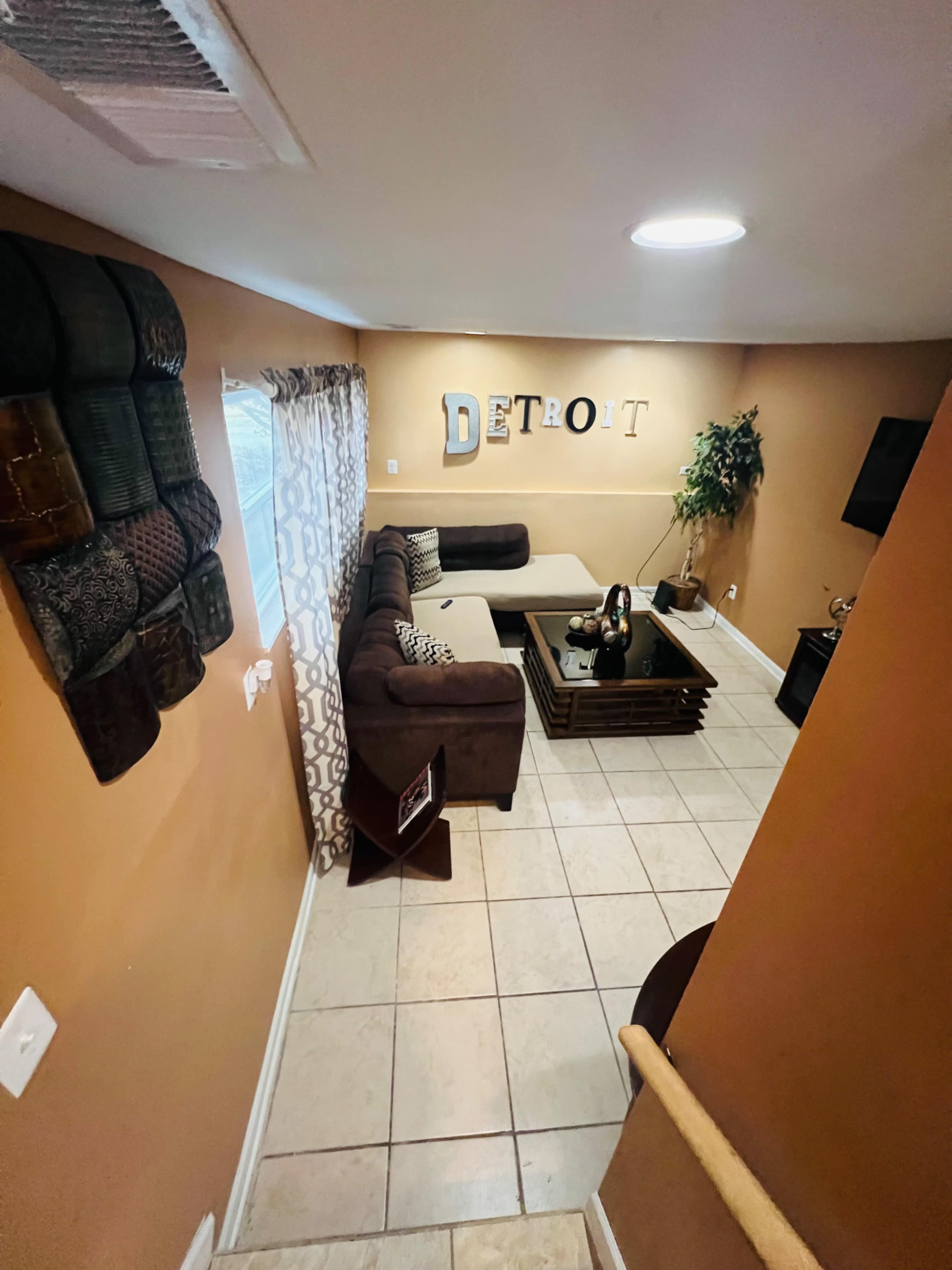 A cozy living room with a sectional couch, a coffee table, and decorative elements on the walls, including the word "Detroit."