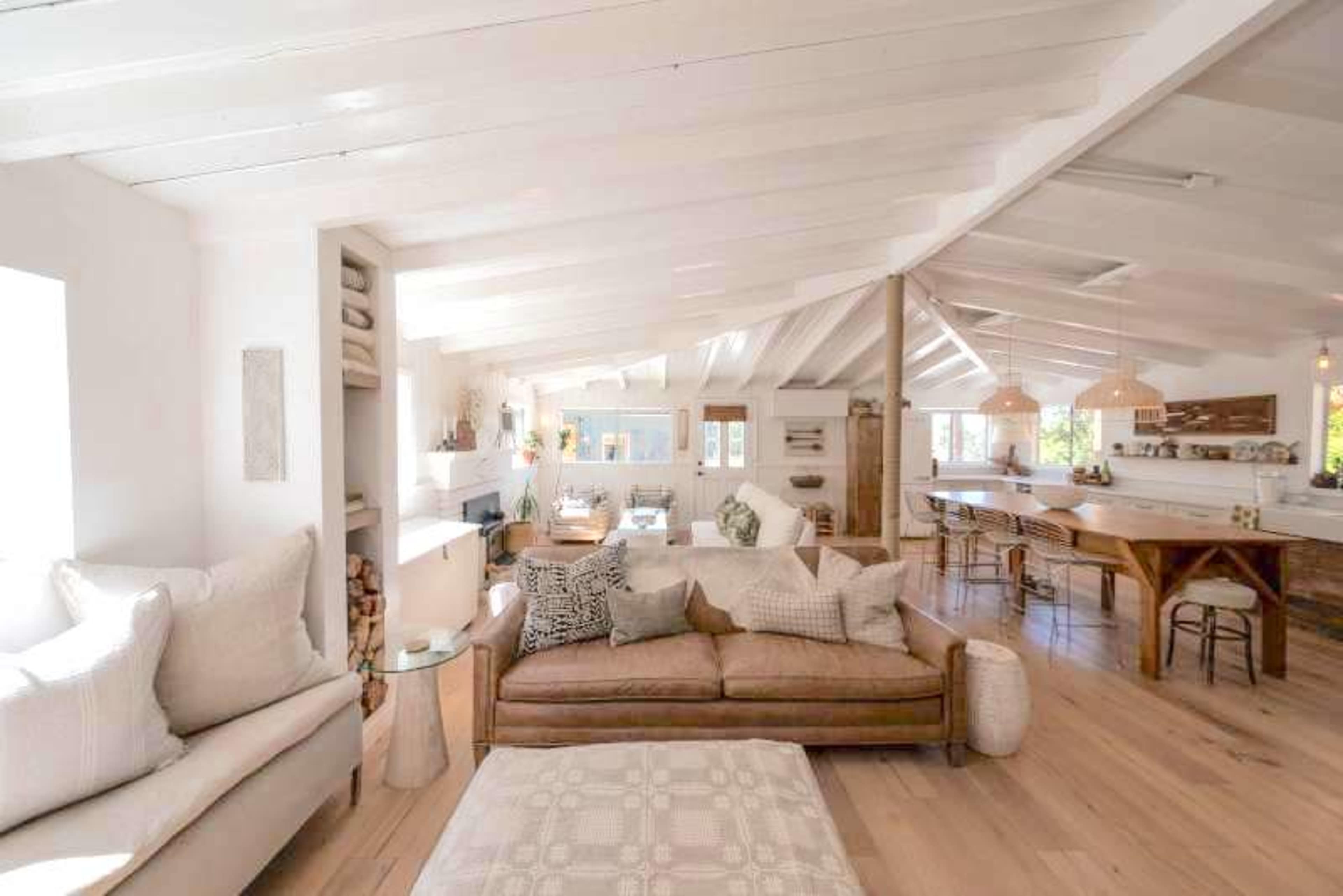 The spacious interior features a living area with a light-colored sofa, wooden floors, and a kitchen bar area.