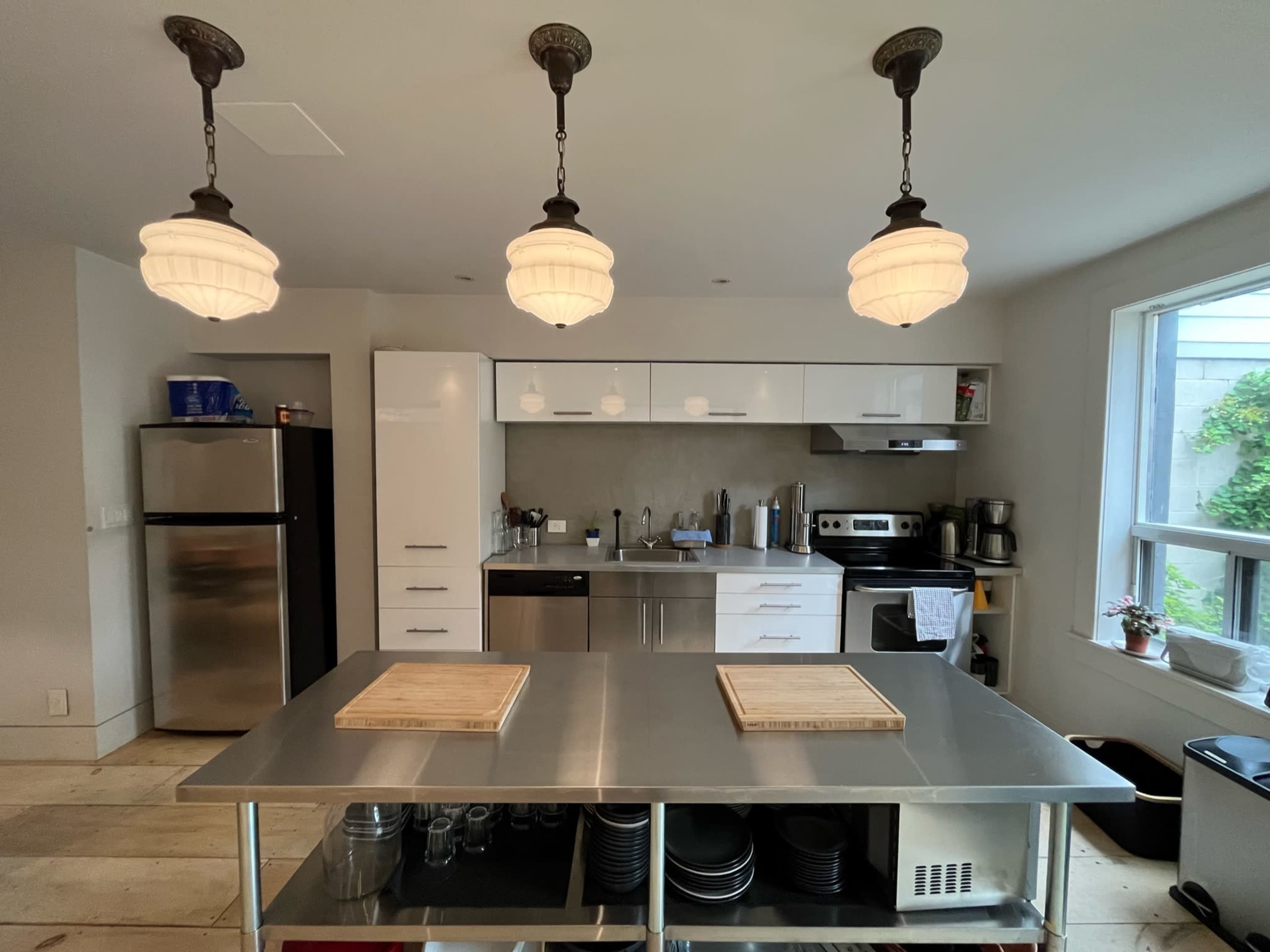 The image shows a modern kitchen featuring a central island with two wooden cutting boards, stainless steel appliances, and three pendant lights hanging above.