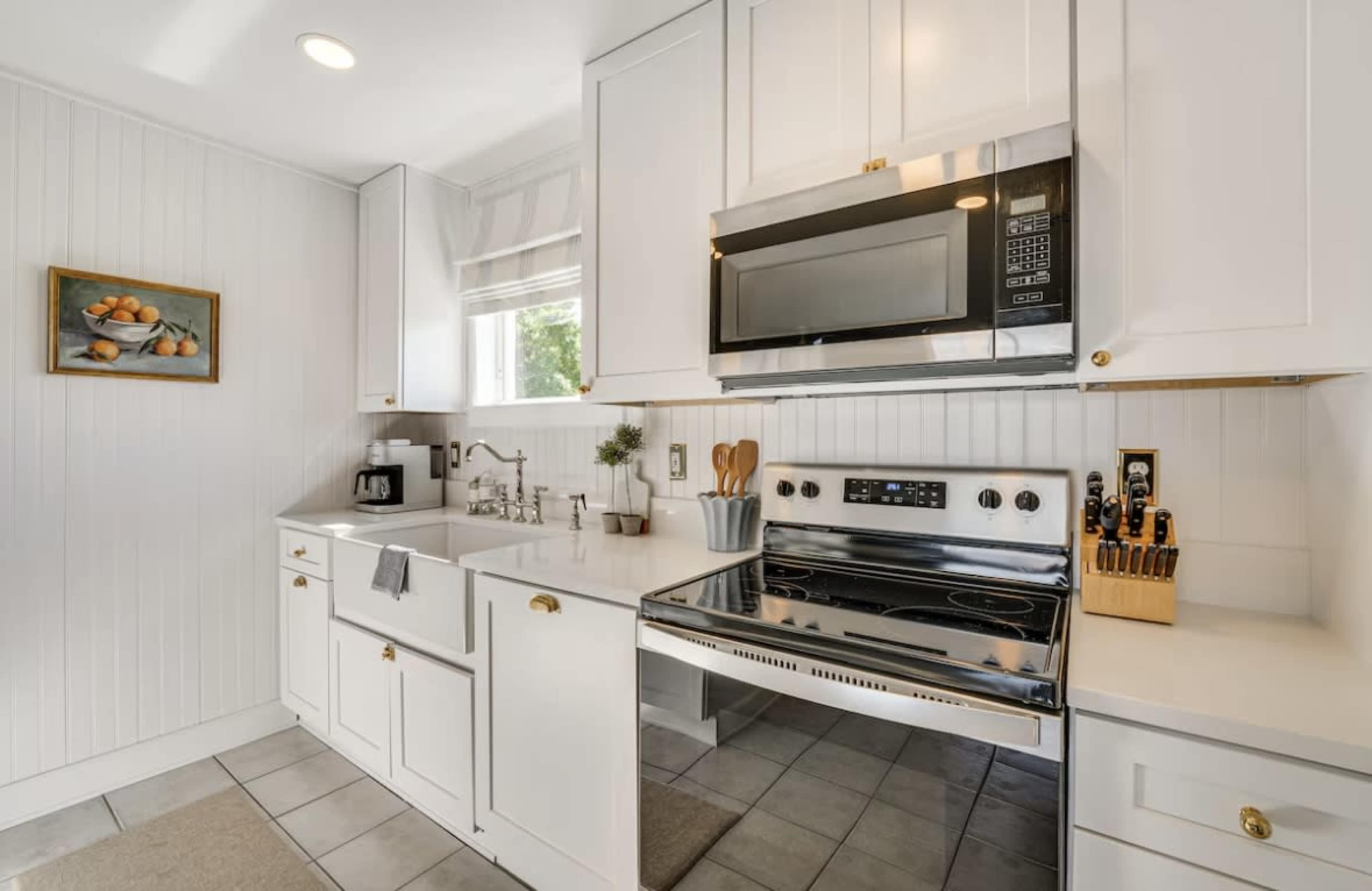 A modern kitchen features white cabinetry, stainless steel appliances, and tiled flooring.