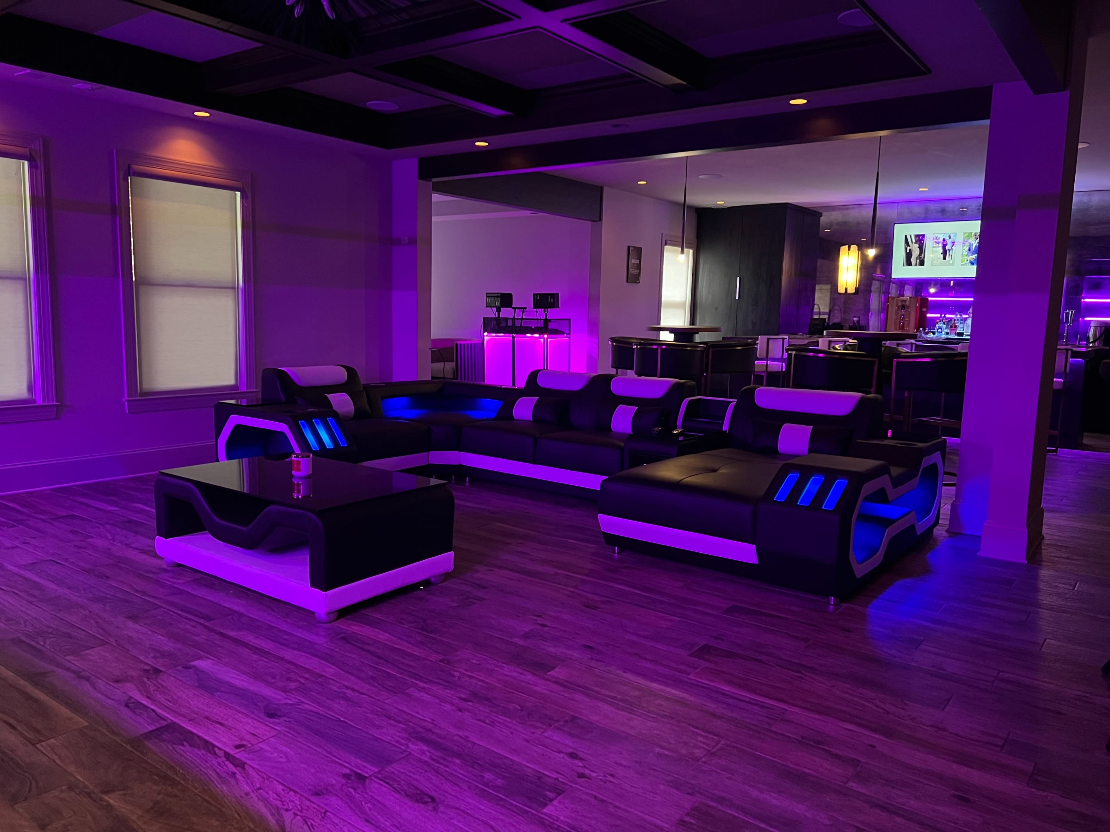 A modern living room featuring a black and white sectional sofa with blue LED lighting and a matching coffee table, set against a backdrop of purple accent lighting.