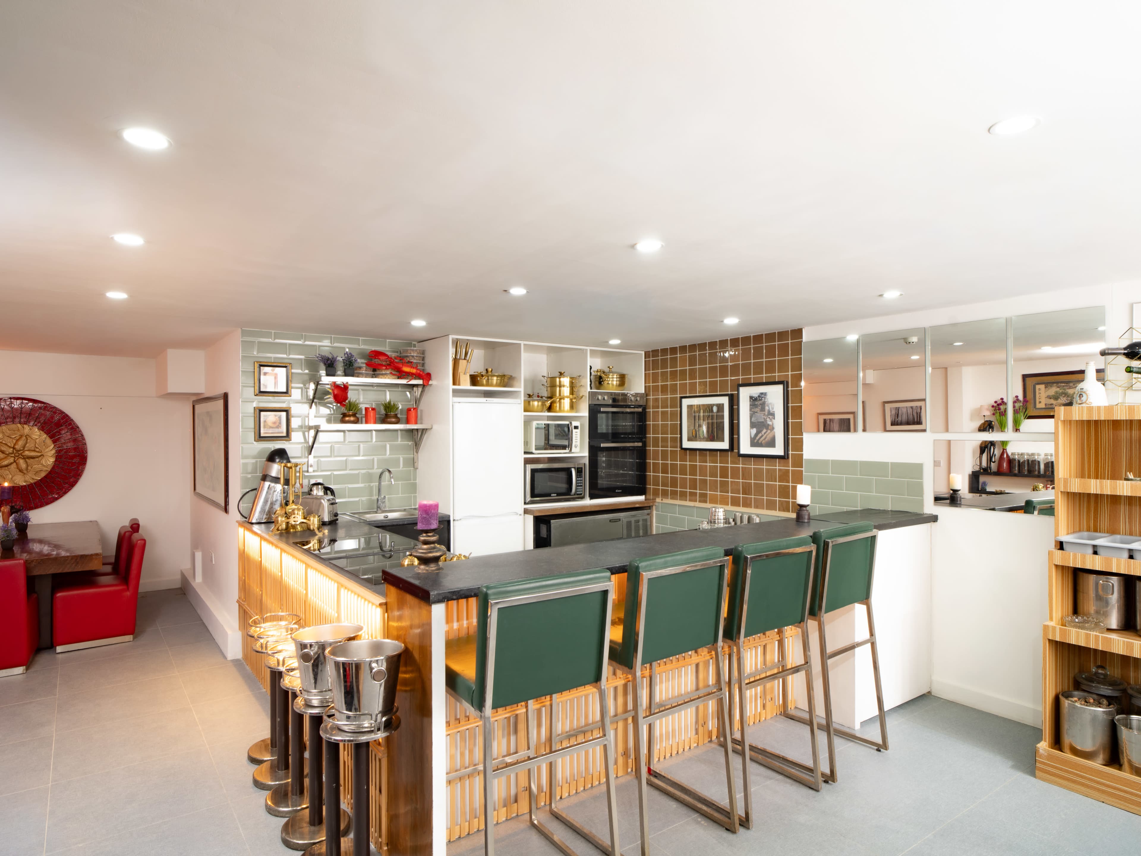 The image shows a modern kitchen with a bar area featuring high stools, stainless steel appliances, and a mix of open shelving and cabinetry.