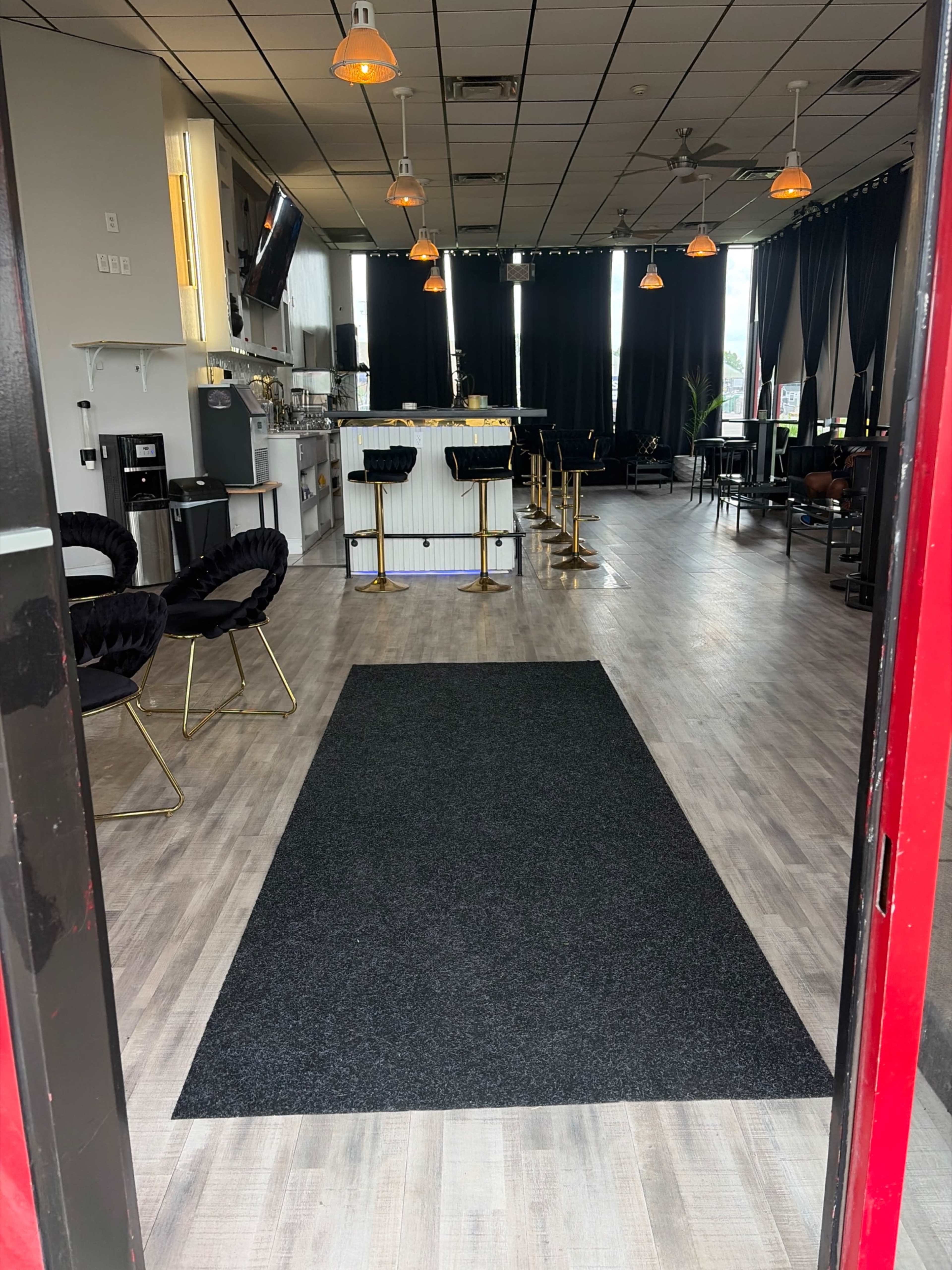 The image shows the interior of a modern restaurant or cafe featuring a black carpet runner leading to a seating area with tables and chairs.