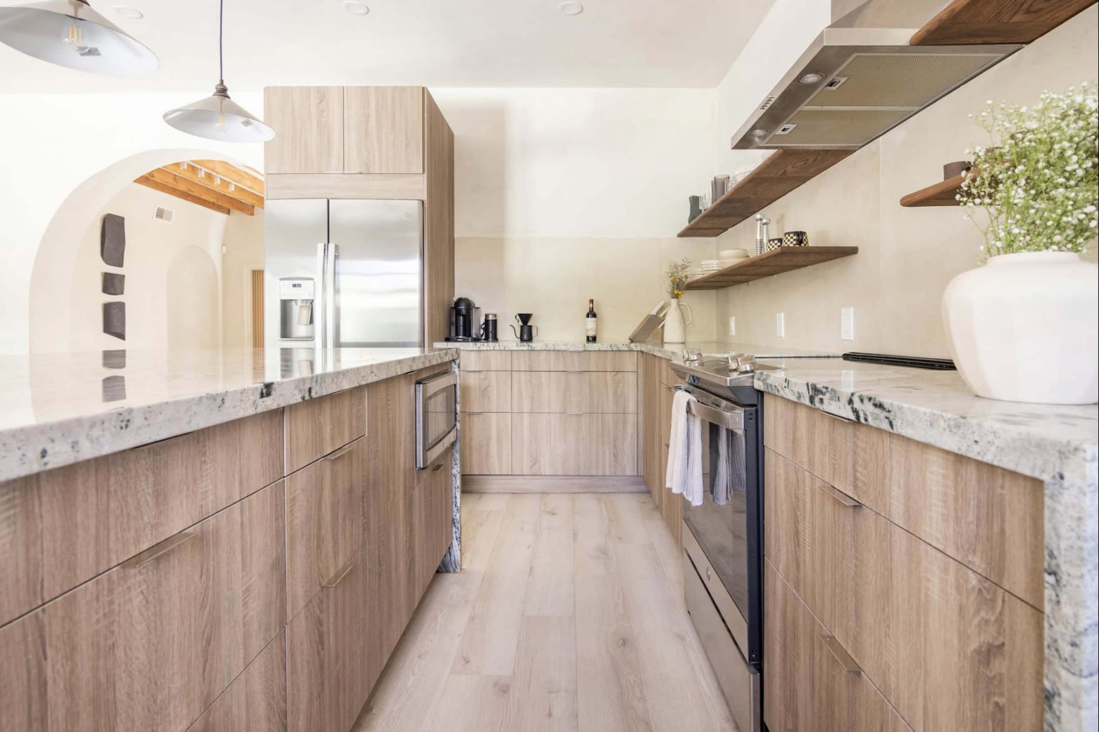 A modern kitchen features wooden cabinetry, a large stone countertop, and stainless steel appliances.
