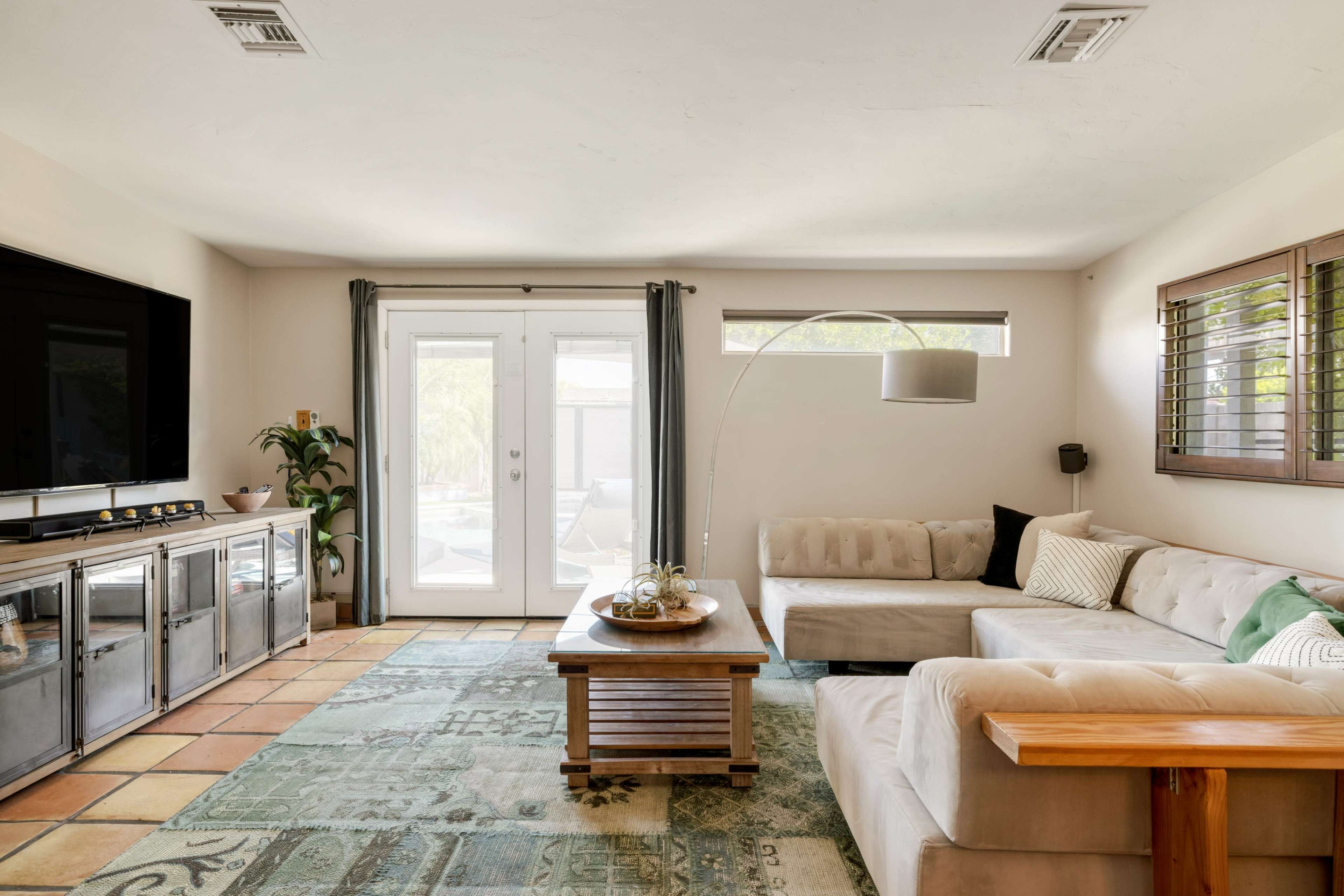 The living room features a sectional sofa, a wooden coffee table, and a large television, with natural light streaming in through the patio doors and windows.