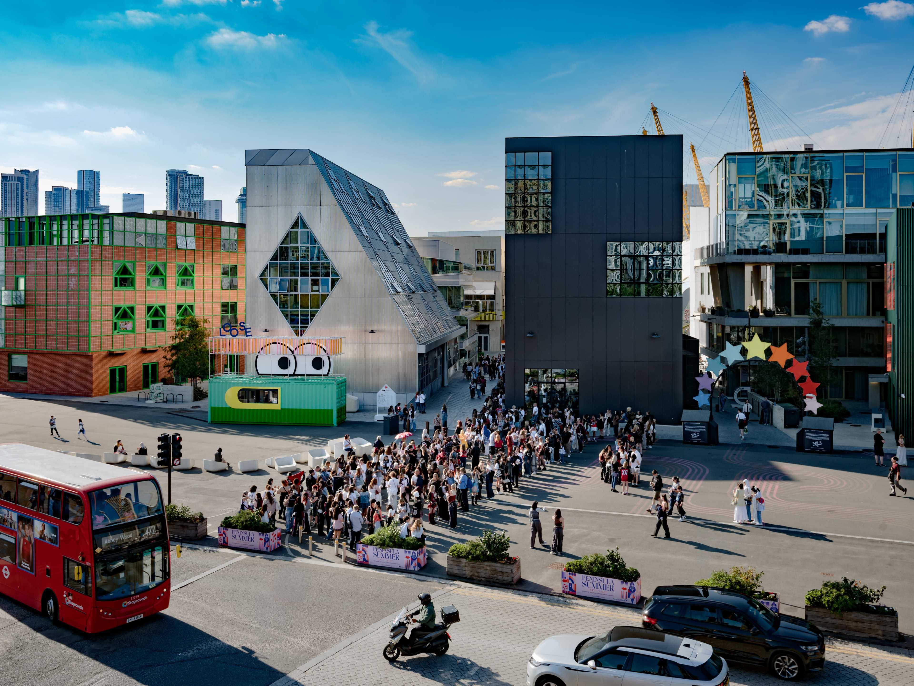 A large crowd gathers outside modern buildings with colorful designs under a clear blue sky.