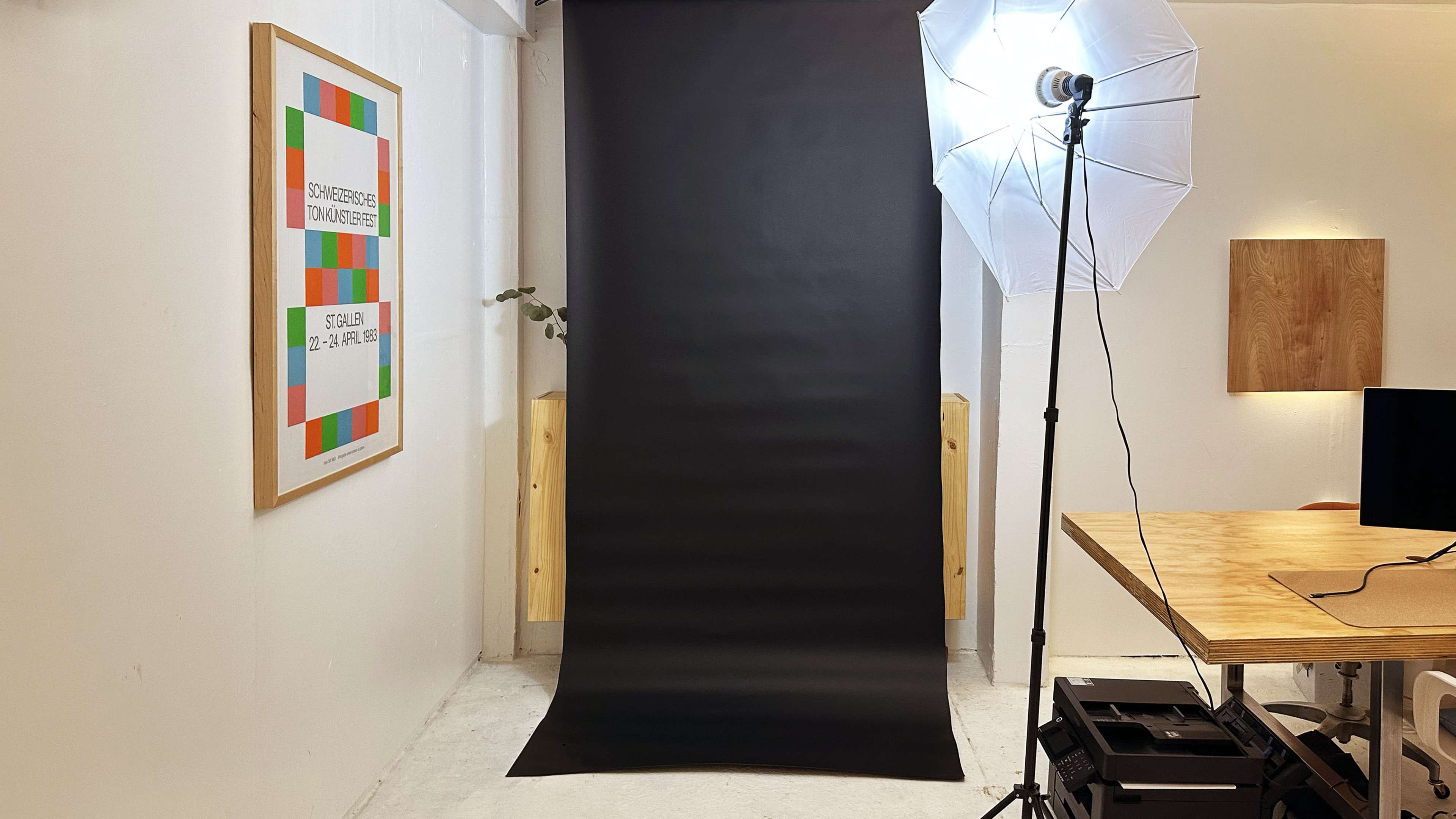 A photography studio setup with a black backdrop, a softbox light, and a wooden table in the corner.