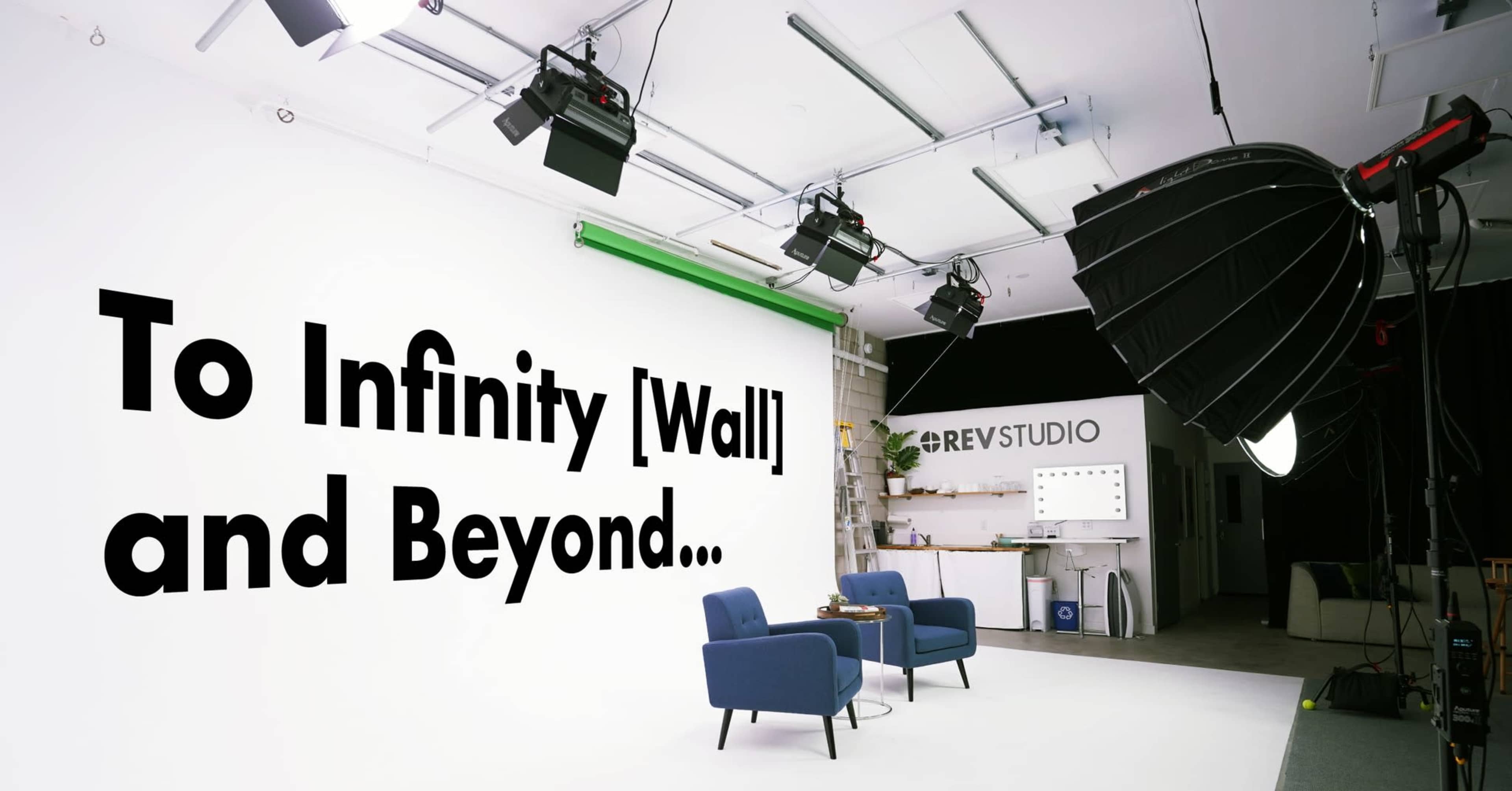 The image shows a brightly lit studio setup featuring a large white wall with the phrase "To Infinity [Wall] and Beyond..." and two blue chairs on a gray floor.
