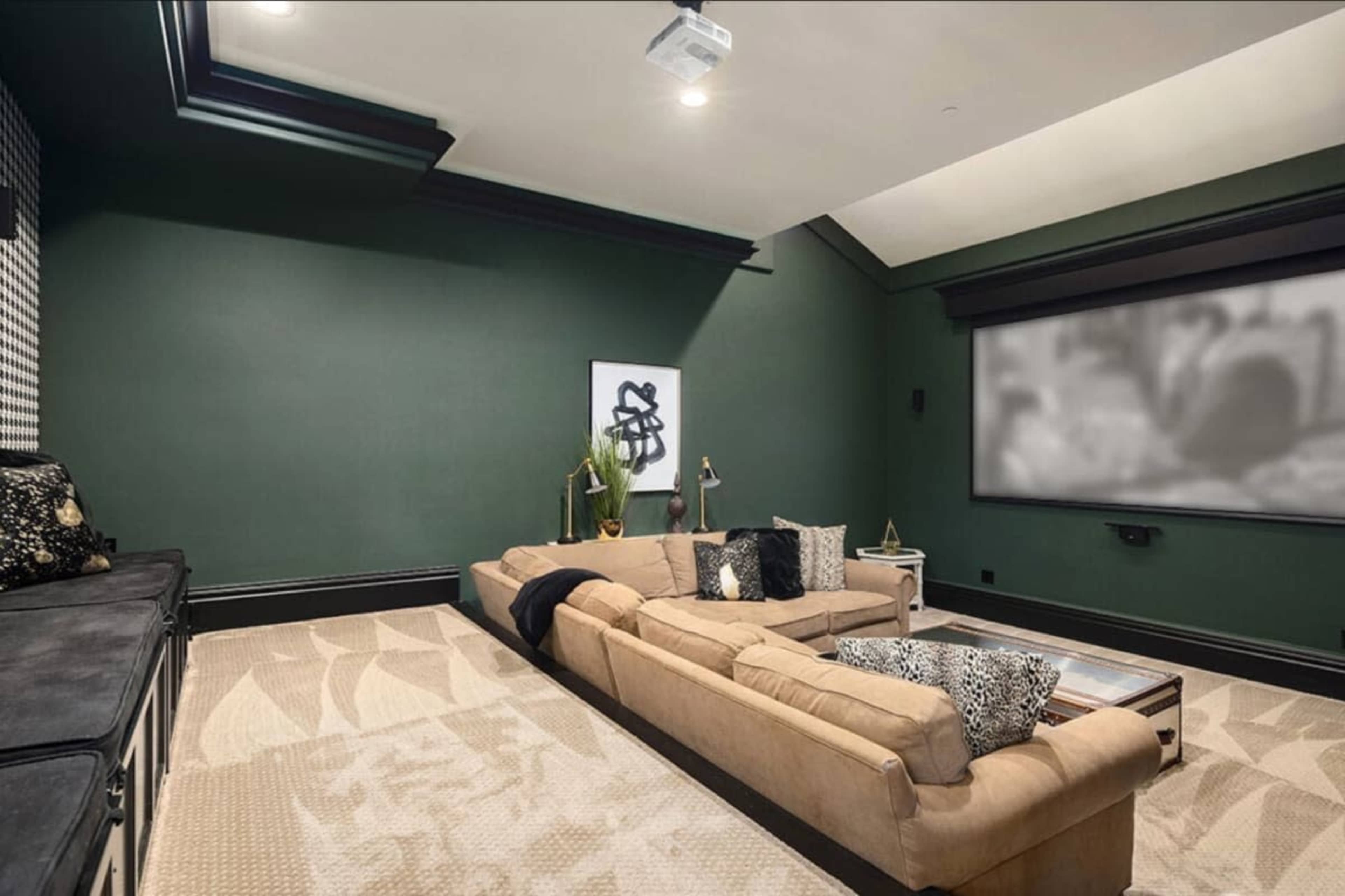 The image depicts a dark-colored home theater room featuring a large sectional sofa, a projector screen, and decorative wall art.