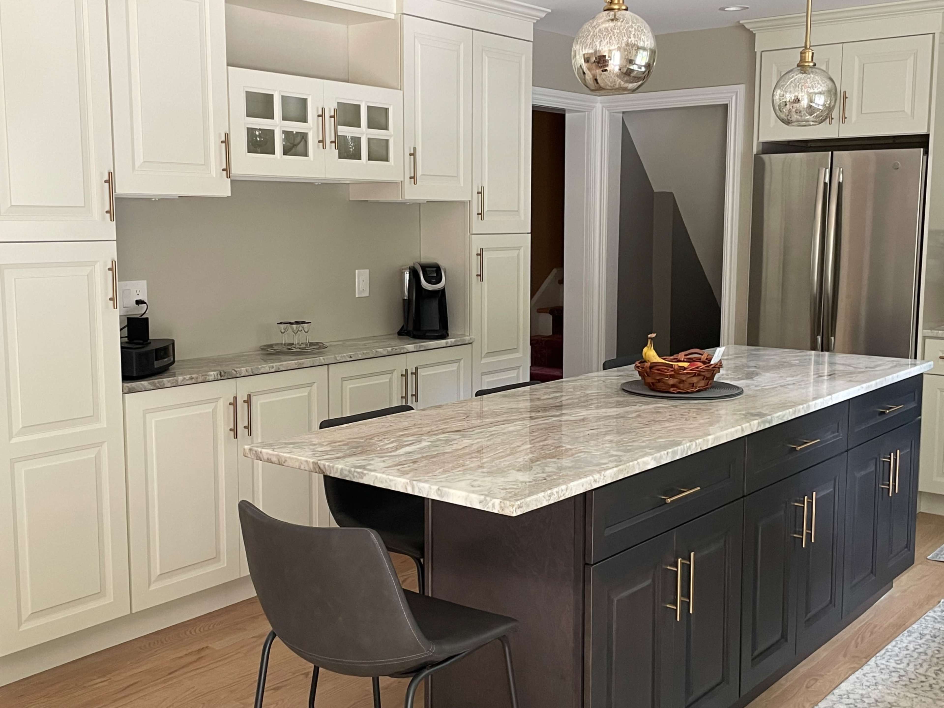 A modern kitchen features white cabinetry, a granite island with seating, and stainless steel appliances.