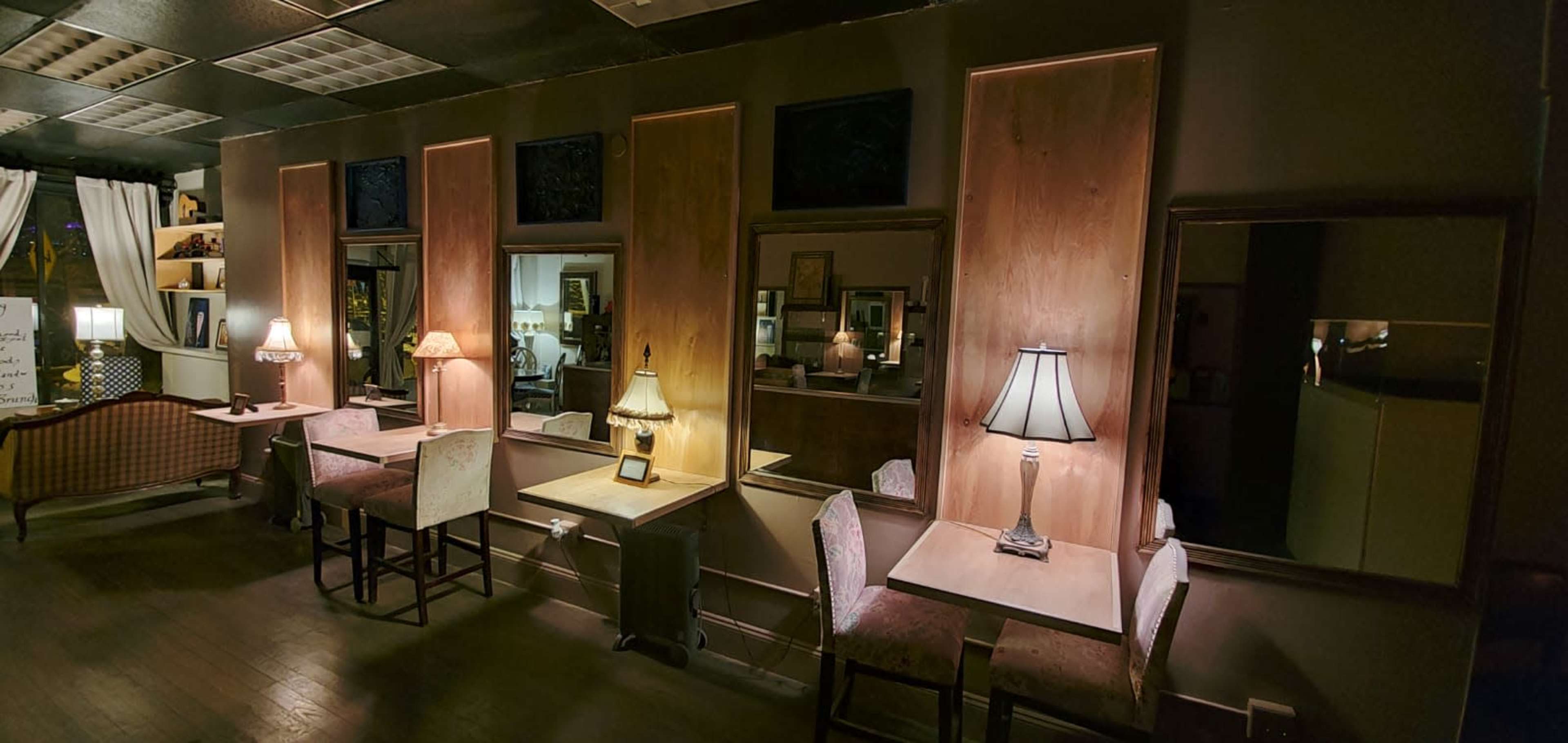 A dimly lit room with wooden paneling, several tables, and lamps, along with mirrors on the walls reflecting the surroundings.