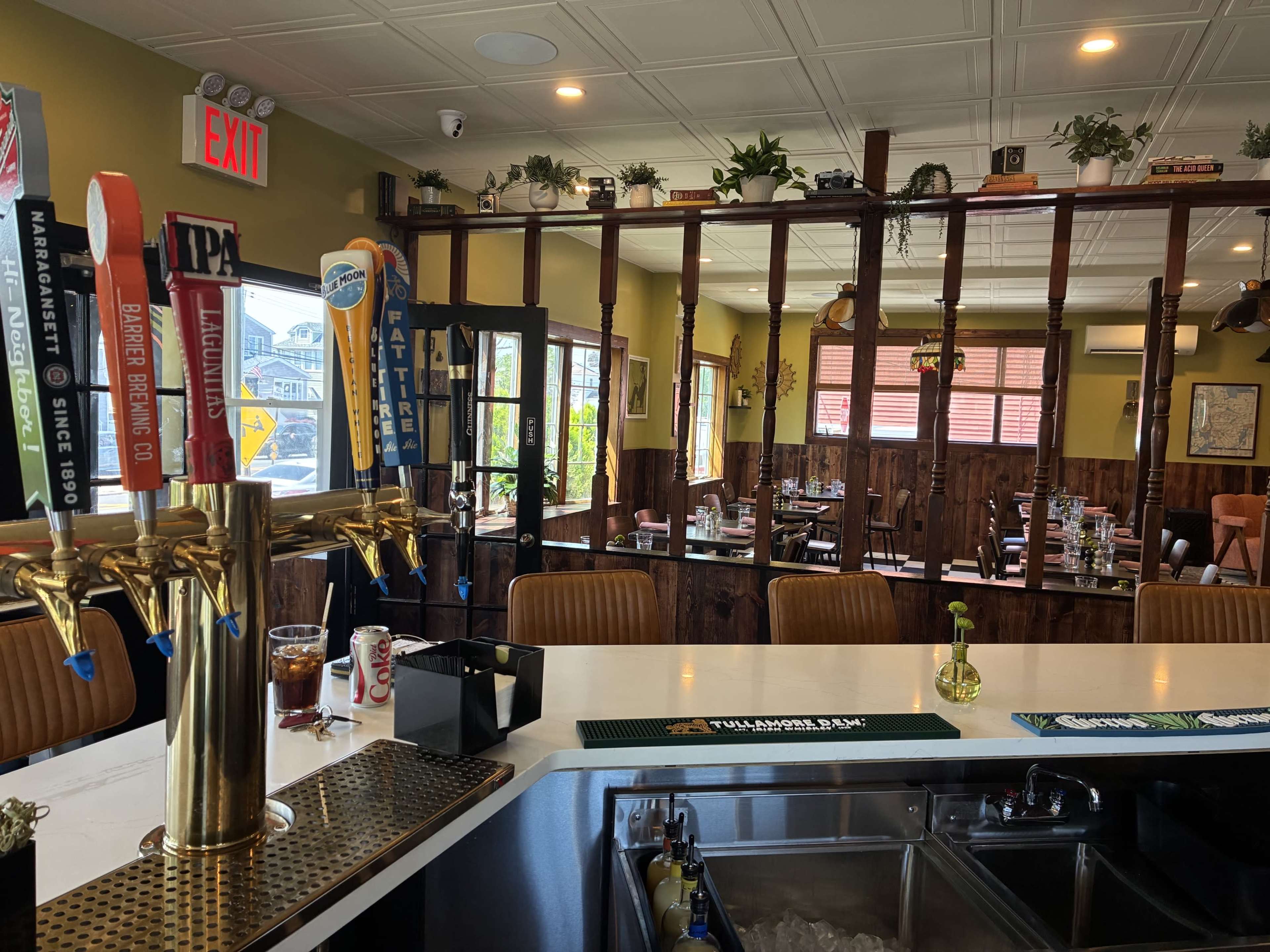 The image shows a bar area with various beer taps and a cozy dining space visible in the background, featuring wooden accents and table settings.