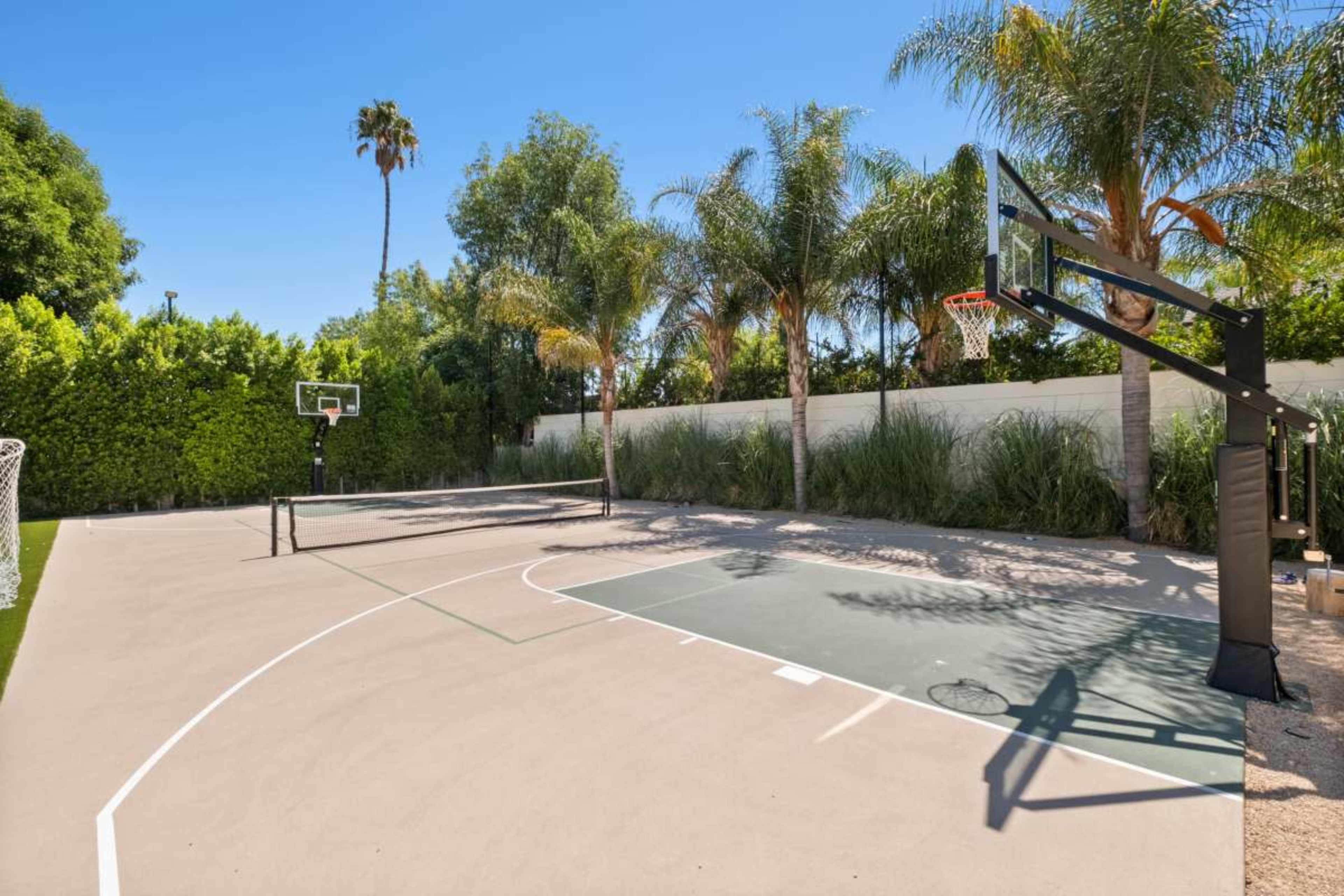 The image shows a well-maintained outdoor basketball court surrounded by palm trees and greenery.